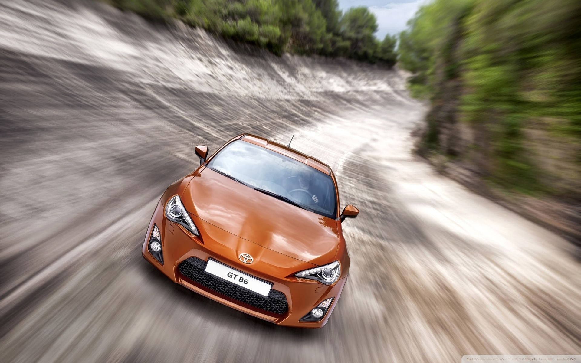 橙色跑車在泥路上飛馳，穿過綠色森林。 — Toyota Supra Mk4 壁紙