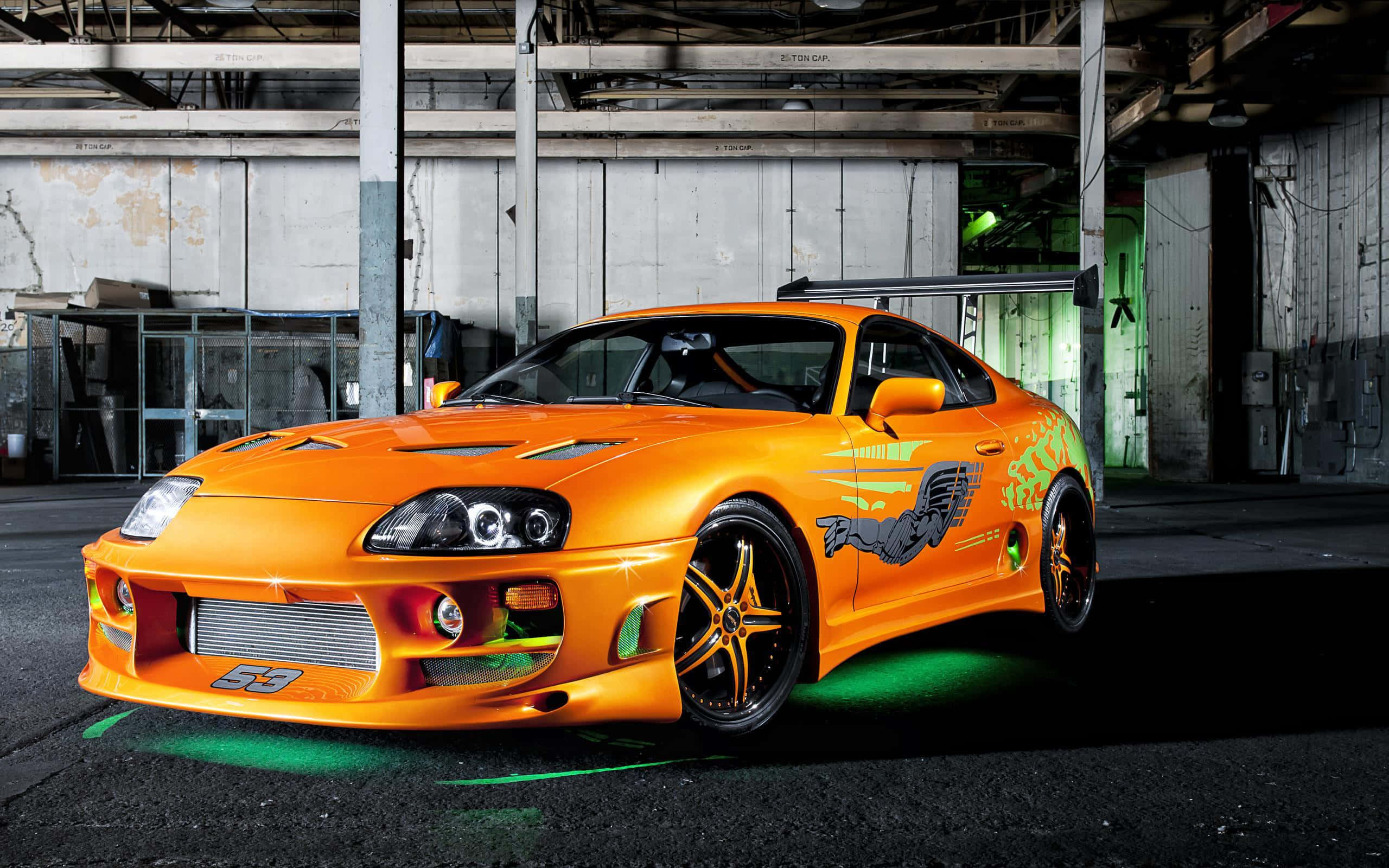 Tuned Car 桌布 壁紙 — 一輛鮮橙色豐田Supra，配有綠色底盤燈和黑色輪圈，停放在骯髒的工業倉庫中。
