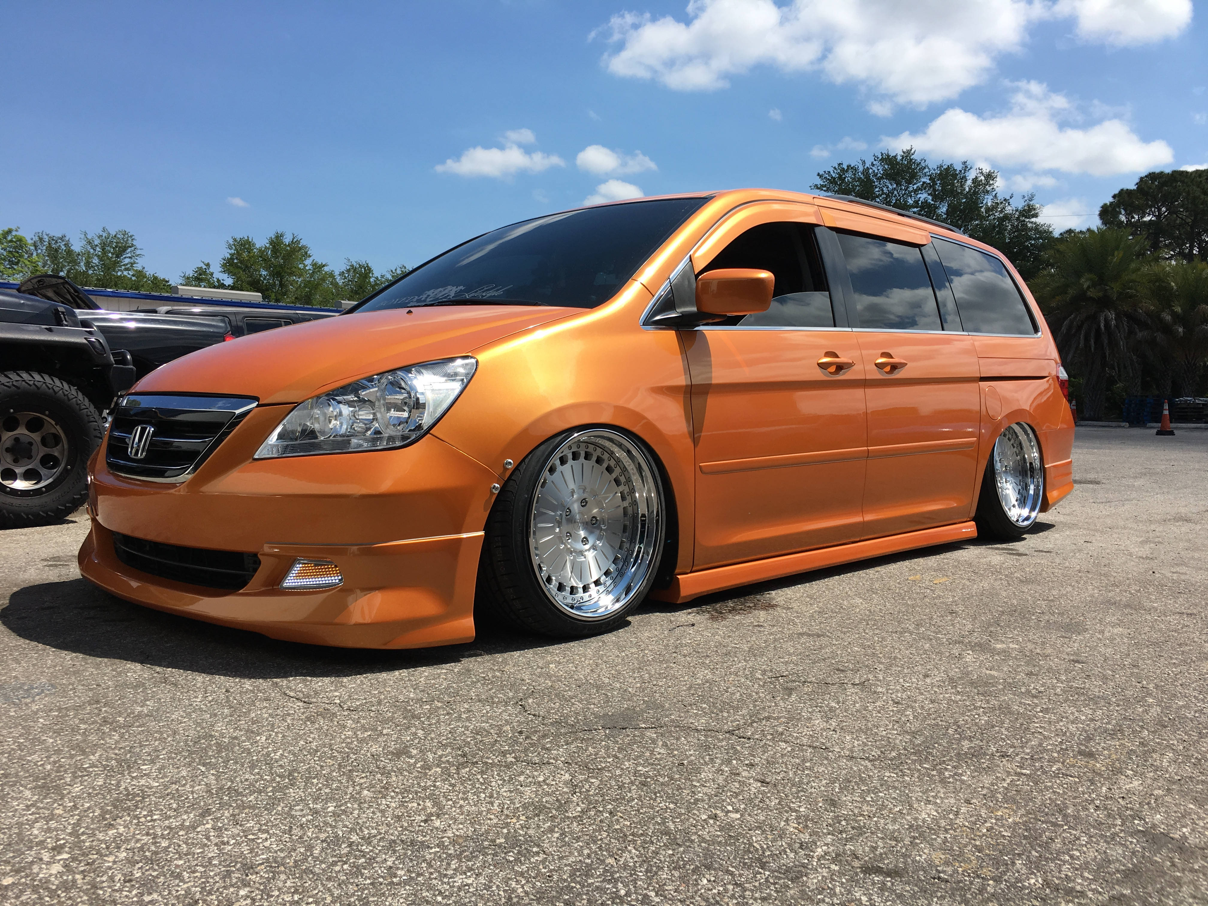 Trucks 桌布 壁紙 — 一輛鮮橙色降低車身的迷你貨車，配備定制鉻合金輪圈，停泊在瀝青路上，天空晴朗藍天白雲。