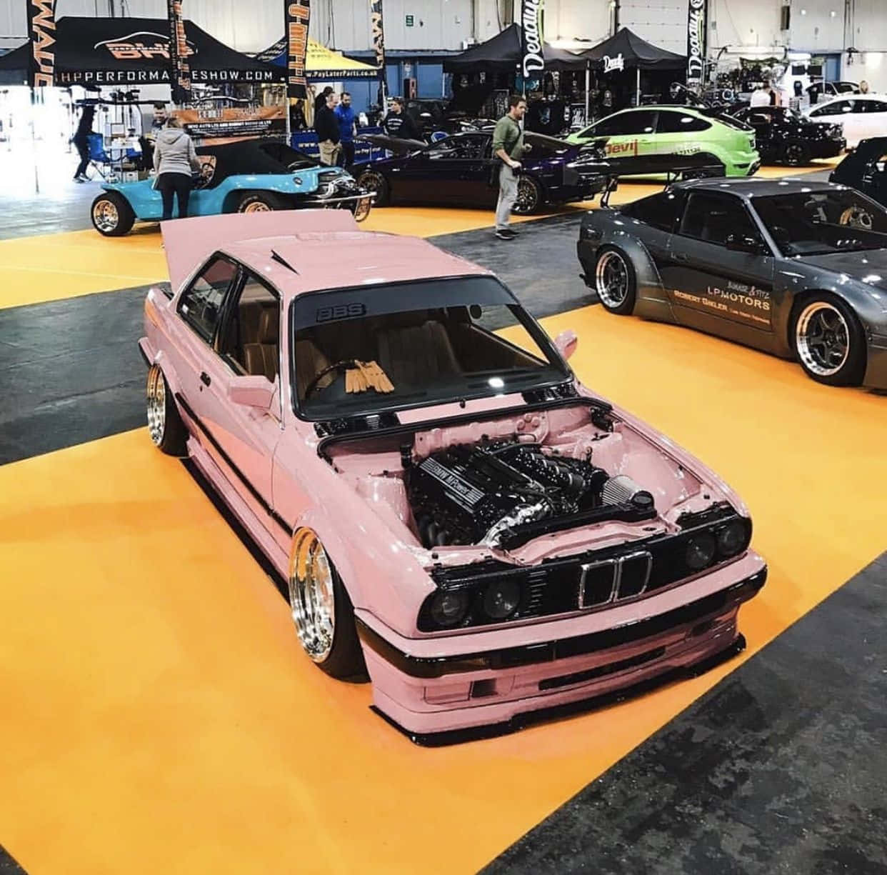 BMW 動圖 桌布 壁紙 — 一輛鮮粉紅色改裝BMW E30打開引擎蓋，在室內車展中展示定制引擎。