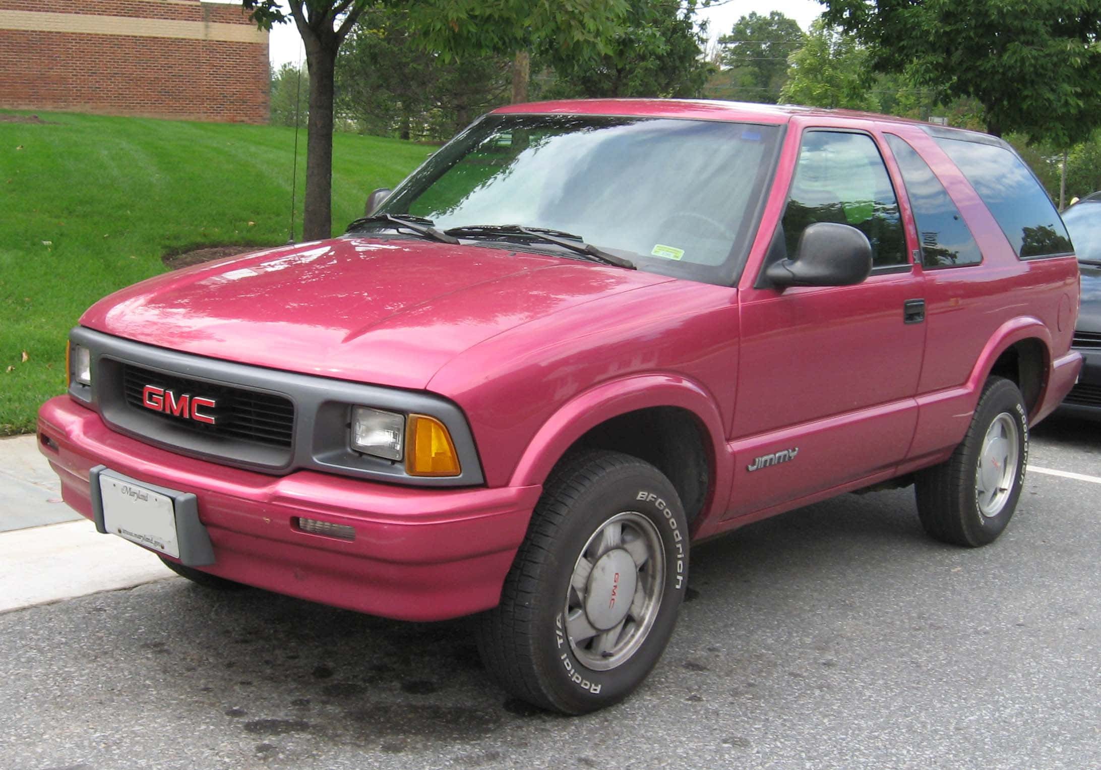 Gmc Jimmy 桌布 壁紙 — 一輛鮮粉紅色的GMC Jimmy SUV停在瀝青路面上，背景有綠草和樹木。