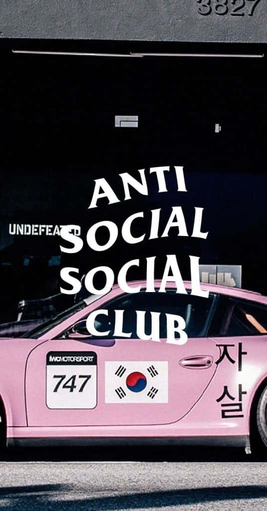 Anti Social Club iPhone 桌布 壁紙 — 一輛鮮粉紅色賽車，帶有「ANTI SOCIAL SOCIAL CLUB」文字和韓國國旗貼紙，停在黑暗的車庫門下。