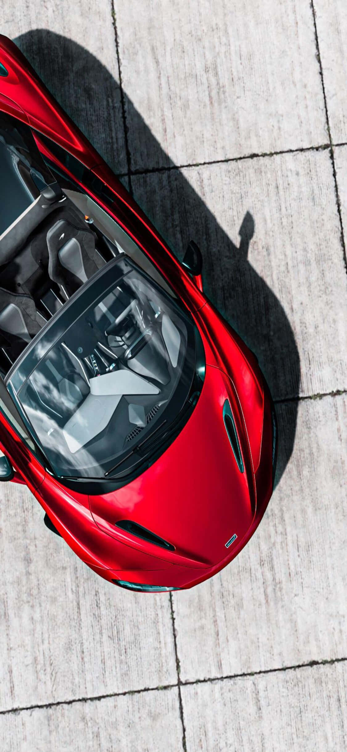 iPhone X Mclaren 720s 桌布 壁紙 — 一輛鮮紅色、帶有流線型敞篷的跑車，停在淺灰色瓷磚表面上，沐浴在明亮的陽光下。
