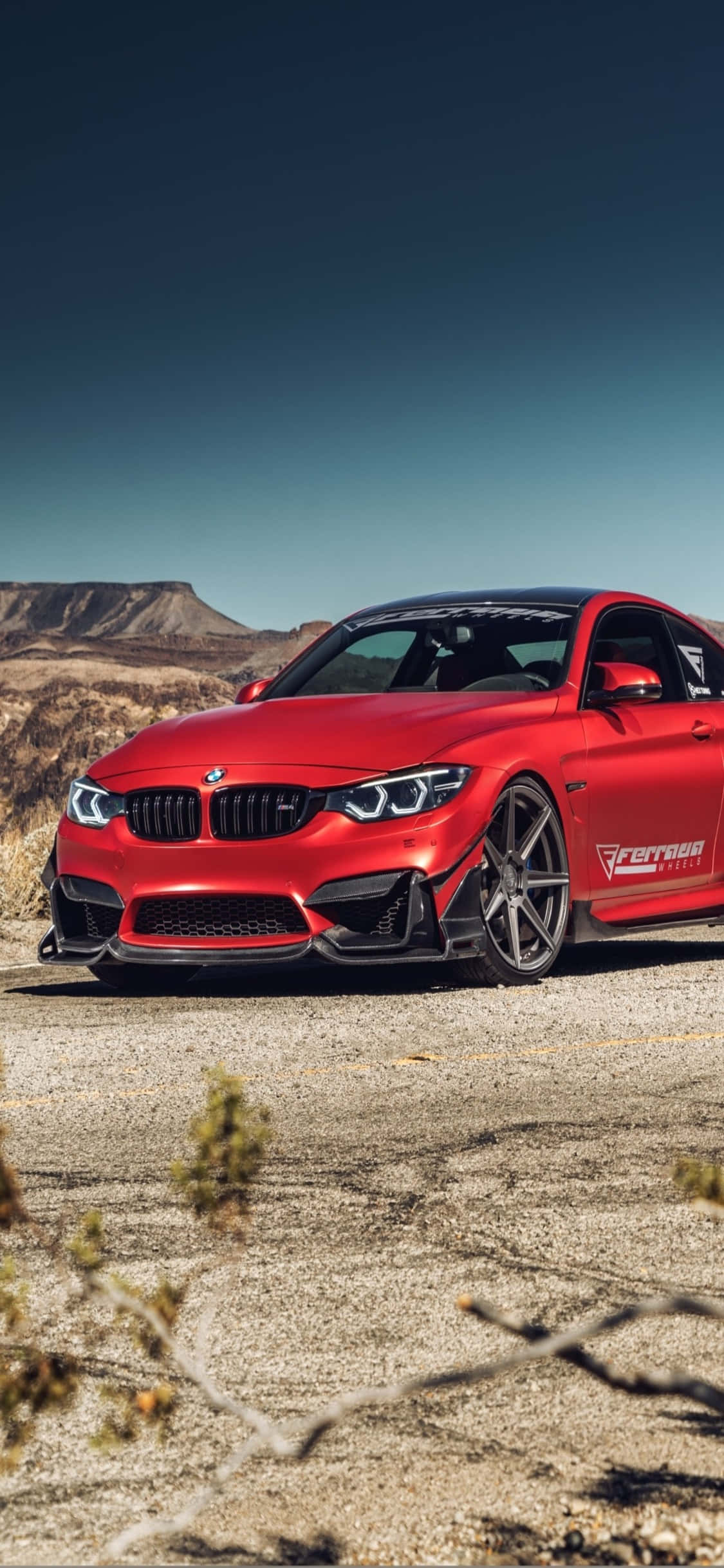 iPhone X Bmw 桌布 壁紙 — 一輛鮮紅色BMW M4雙門轎跑車，帶黑色飾件，停泊在龜裂的沙漠地面上，天空湛藍清澈。