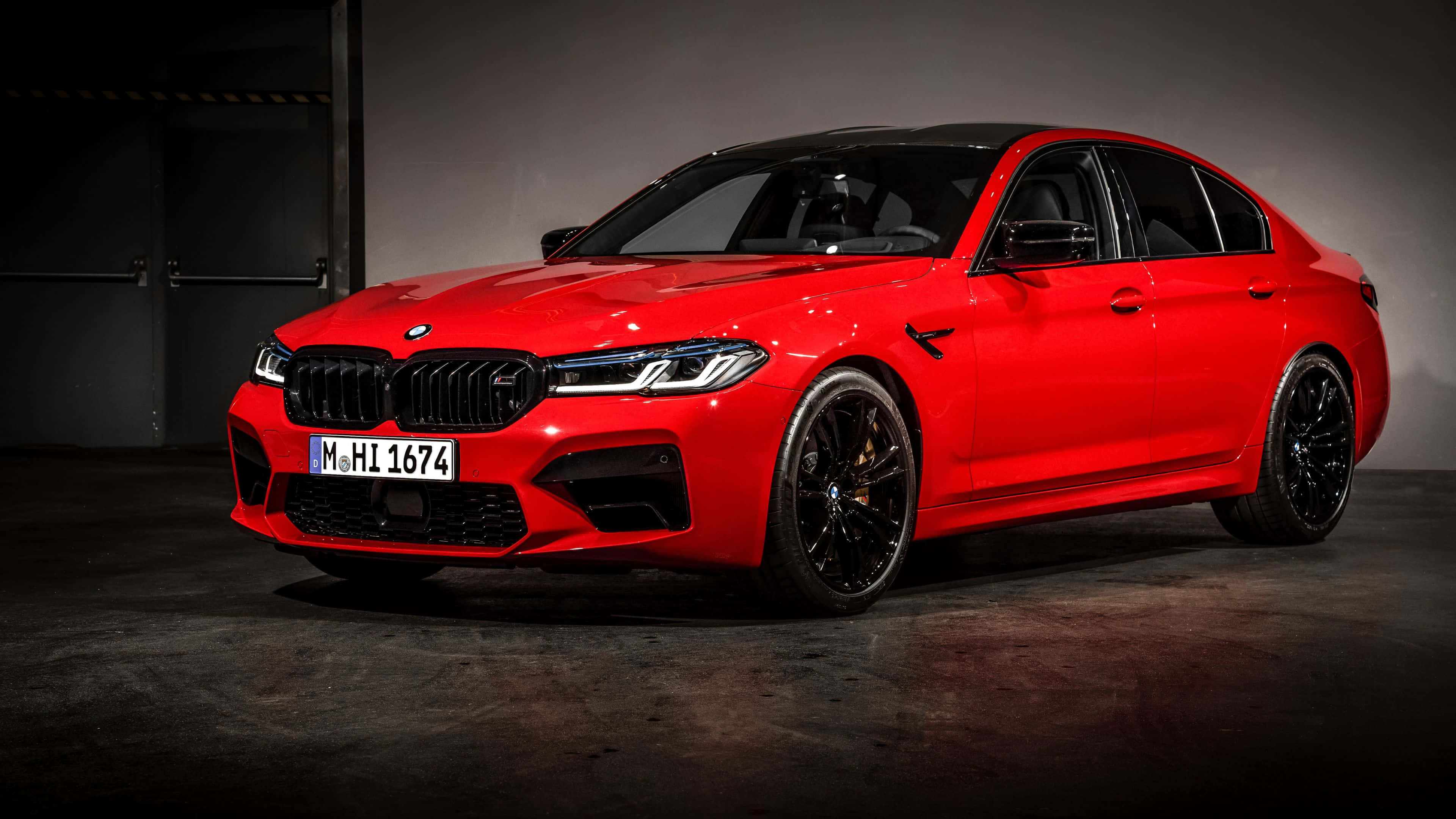 4K BMW 壁紙 桌布 壁紙 — 一輛鮮紅色BMW M5轎車，帶有黑色飾件和光澤表面，在光線昏暗的工業車庫中展示。