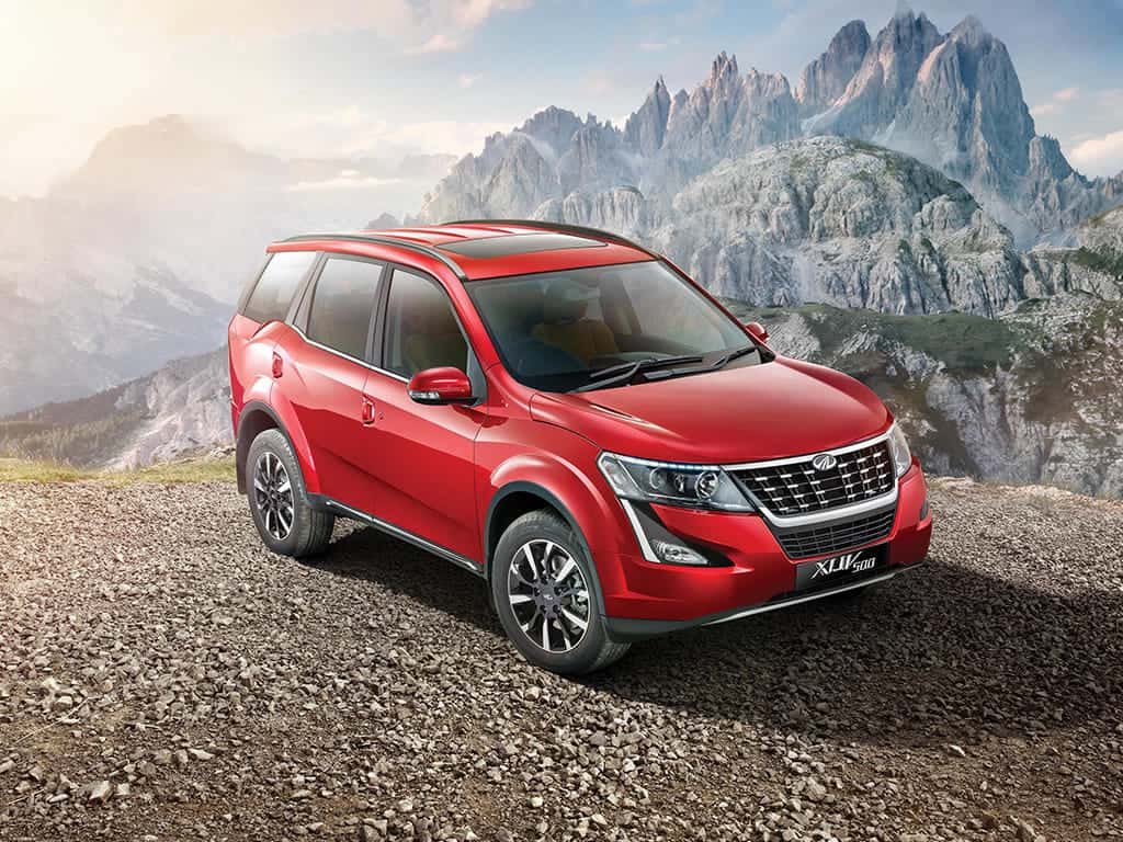 Mahindra 桌布 壁紙 — 一輛鮮紅色SUV停泊在岩石山隘，背後鋸齒狀山峰在柔和晨空下聳立。
