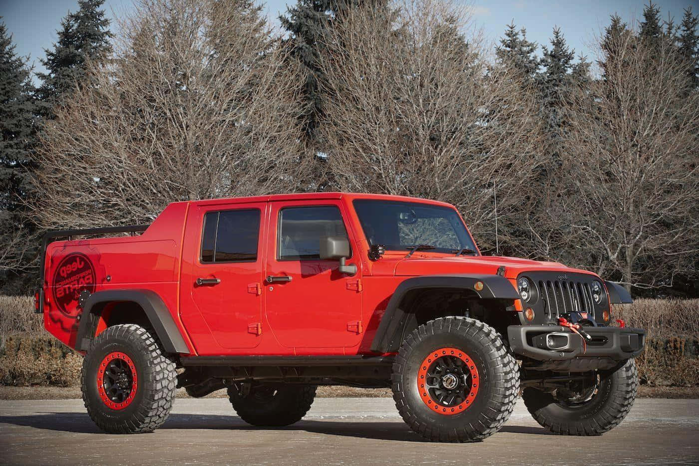 Jeep Gladiator 桌布 壁紙 — 一輛鮮紅色升高的Jeep Wrangler，配備超大輪胎，大膽地站在鋪砌的路面上，周圍是光禿禿的冬天樹木。
