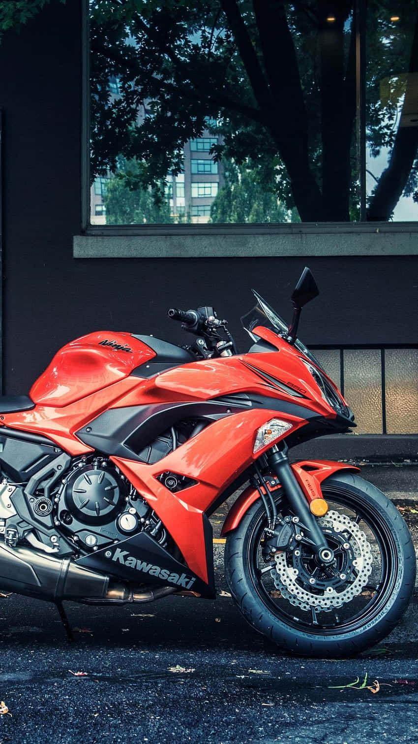 Kawasaki Desktop 桌布 壁紙 — 一輛鮮紅色川崎運動機車停在濕滑路面上，旁邊是現代建築，窗戶反射出樹木的倒影。