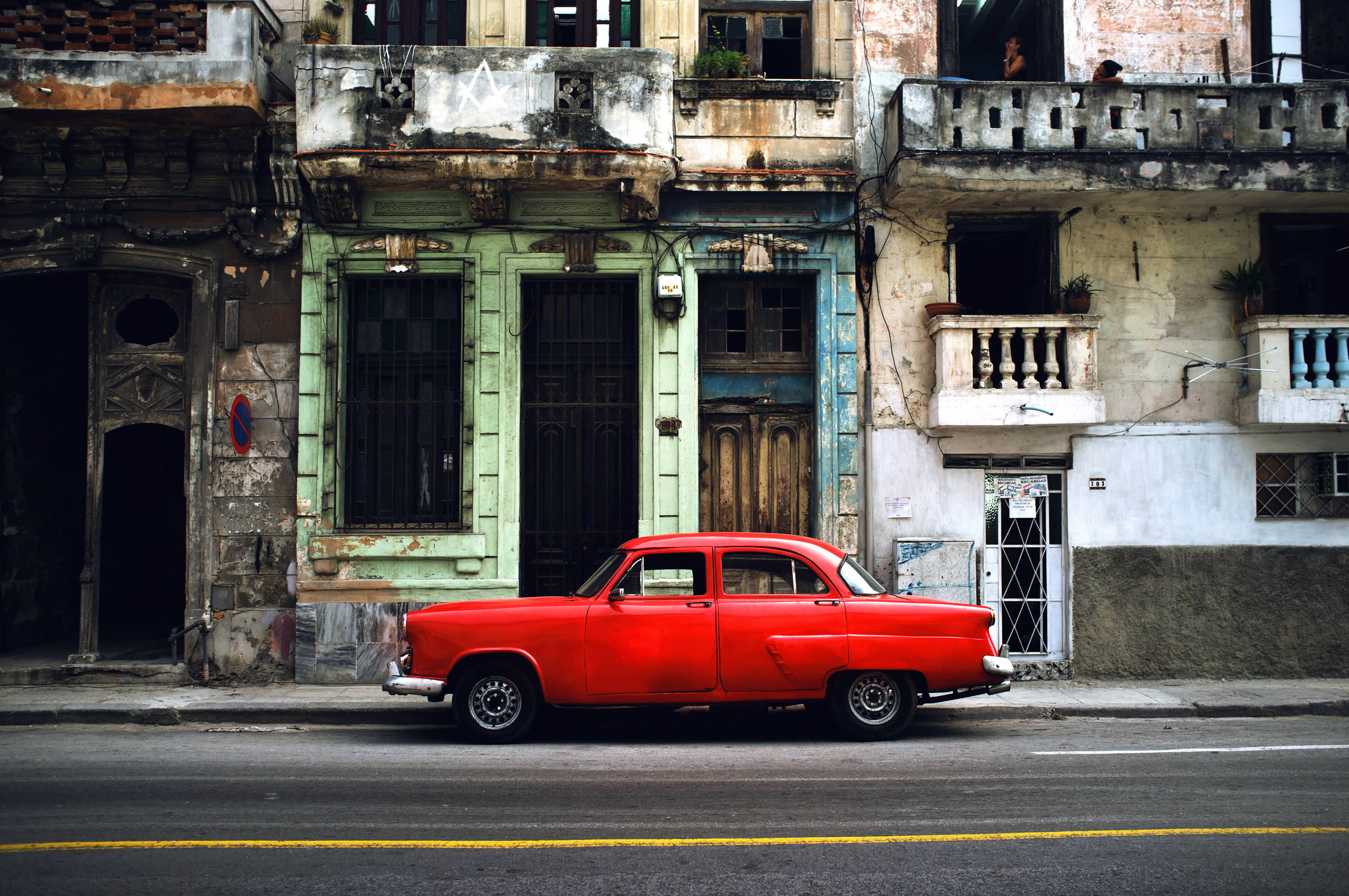 Cuba 桌布 壁紙 — 一輛鮮紅色復古車停在風化的街道上，旁邊是油漆剝落、帶有鍛鐵陽台的破舊殖民時期建築。