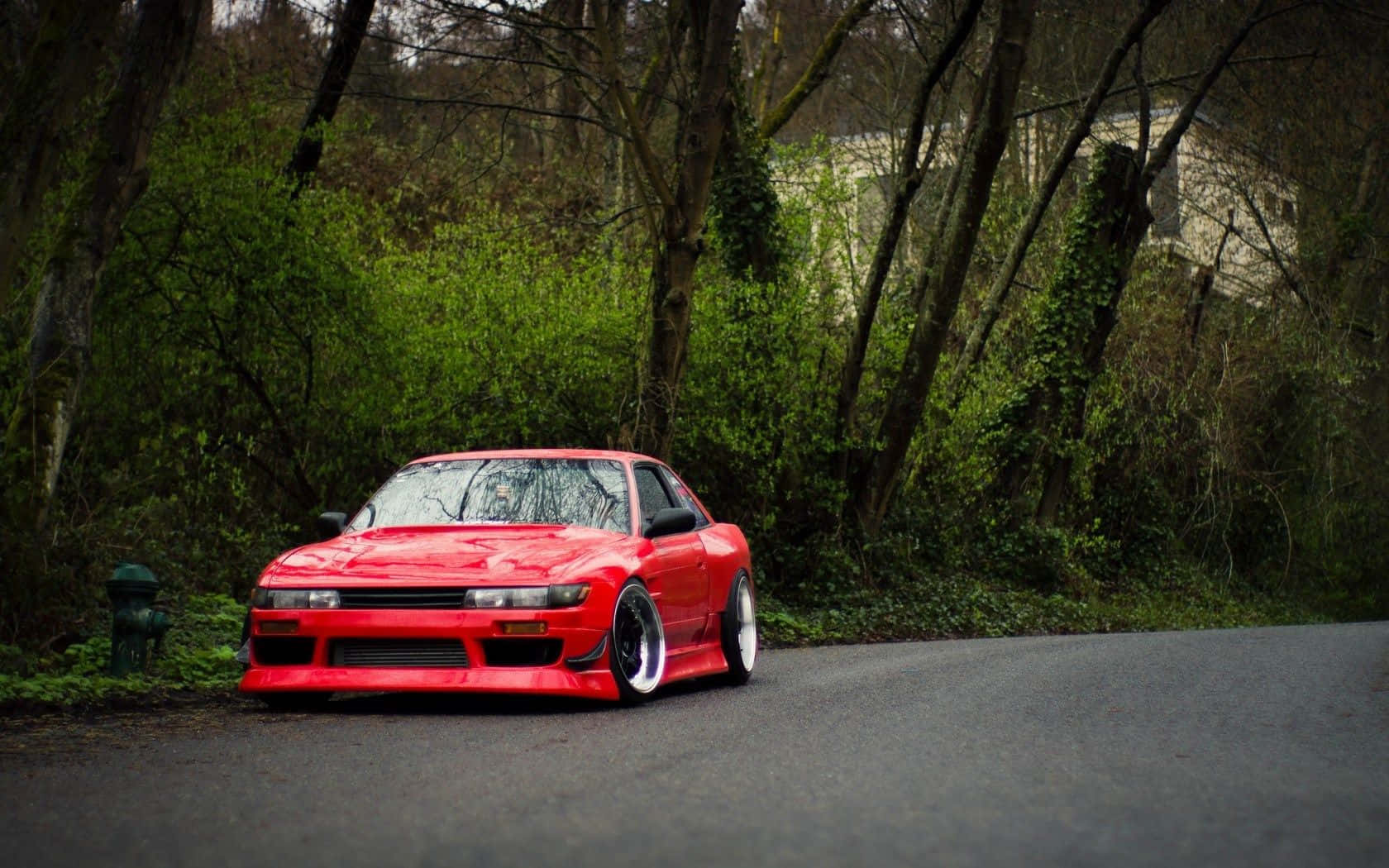 Nissan Silvia S13 桌布 壁紙 — 一輛鮮紅色改裝跑車停泊在蜿蜒的森林道路上，周圍是茂密的綠色樹葉。