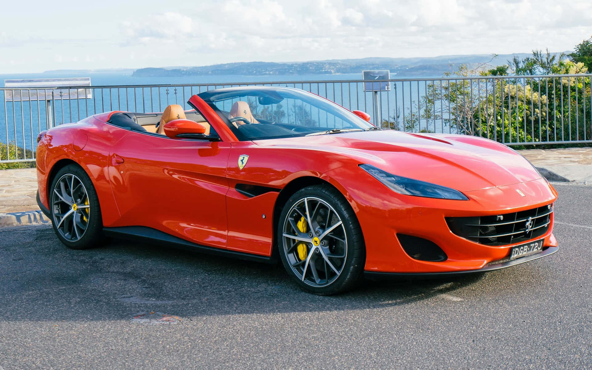 Ferrari Portofino 桌布 壁紙 — 一輛鮮紅色法拉利Portofino敞篷跑車停在海邊觀景點，可欣賞海景，車內有兩人。