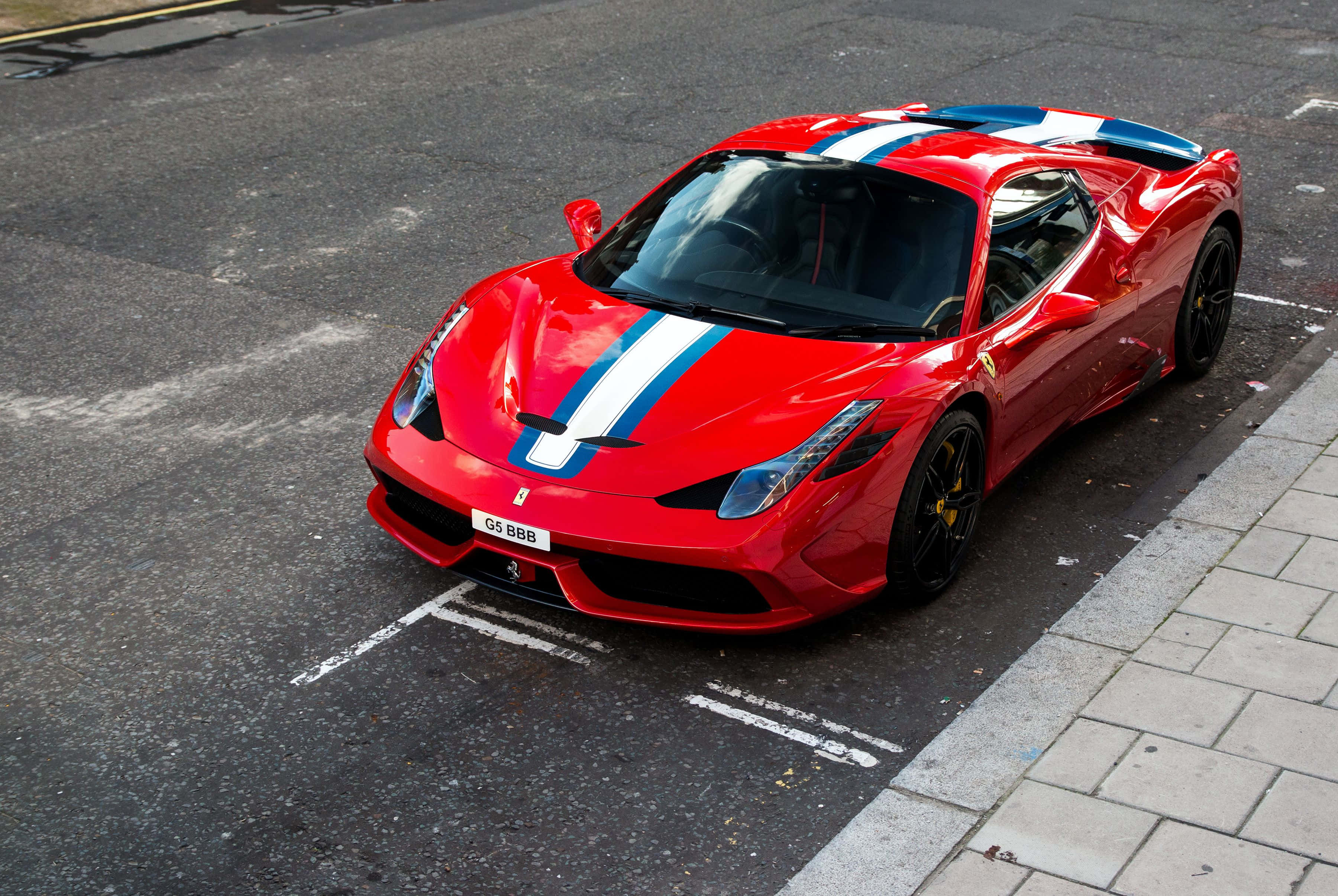 Ferrari 458 Speciale 桌布 壁紙 — 一輛鮮紅色法拉利跑車，帶有藍白賽車條紋，停在城市街道上。