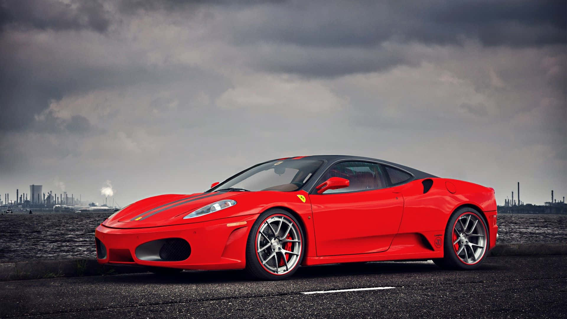 Ferrari F430 桌布 壁紙 — 一輛鮮紅色法拉利跑車停在柏油路上，背景是戲劇性的多雲天空和遠處的工業建築。