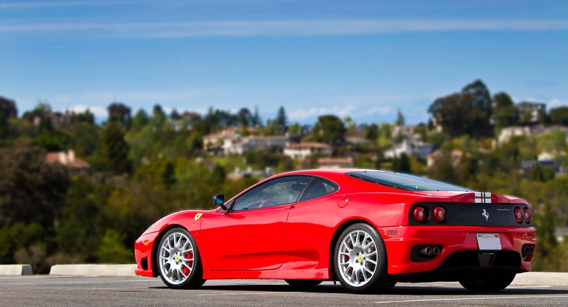 Ferrari 360 Modena 桌布 壁紙 — 一輛鮮紅色法拉利跑車停泊在陽光明媚的高速公路上，俯瞰著綠草如茵、房屋林立的丘陵。