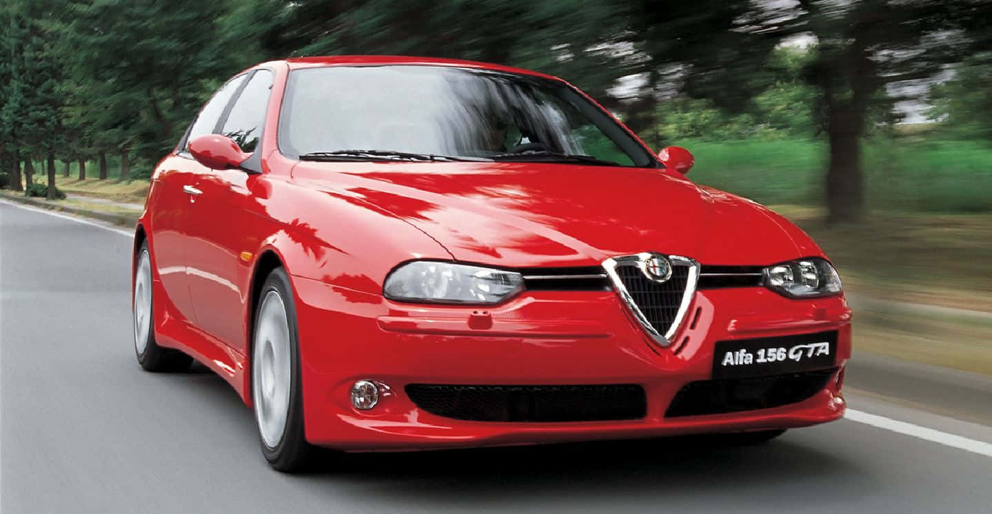 Alfa Romeo 156 桌布 壁紙 — 一輛鮮紅色的 Alfa 156 GTA 在綠樹成蔭的道路上疾馳，動態模糊傳達出動感。