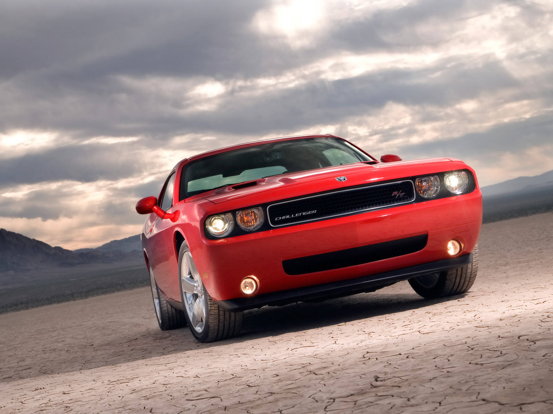 Challenger 桌布 壁紙 — 一輛鮮紅色的 Dodge Challenger SRT8 在戲劇性的多雲天空下，大膽地矗立在龜裂的沙漠地面上。