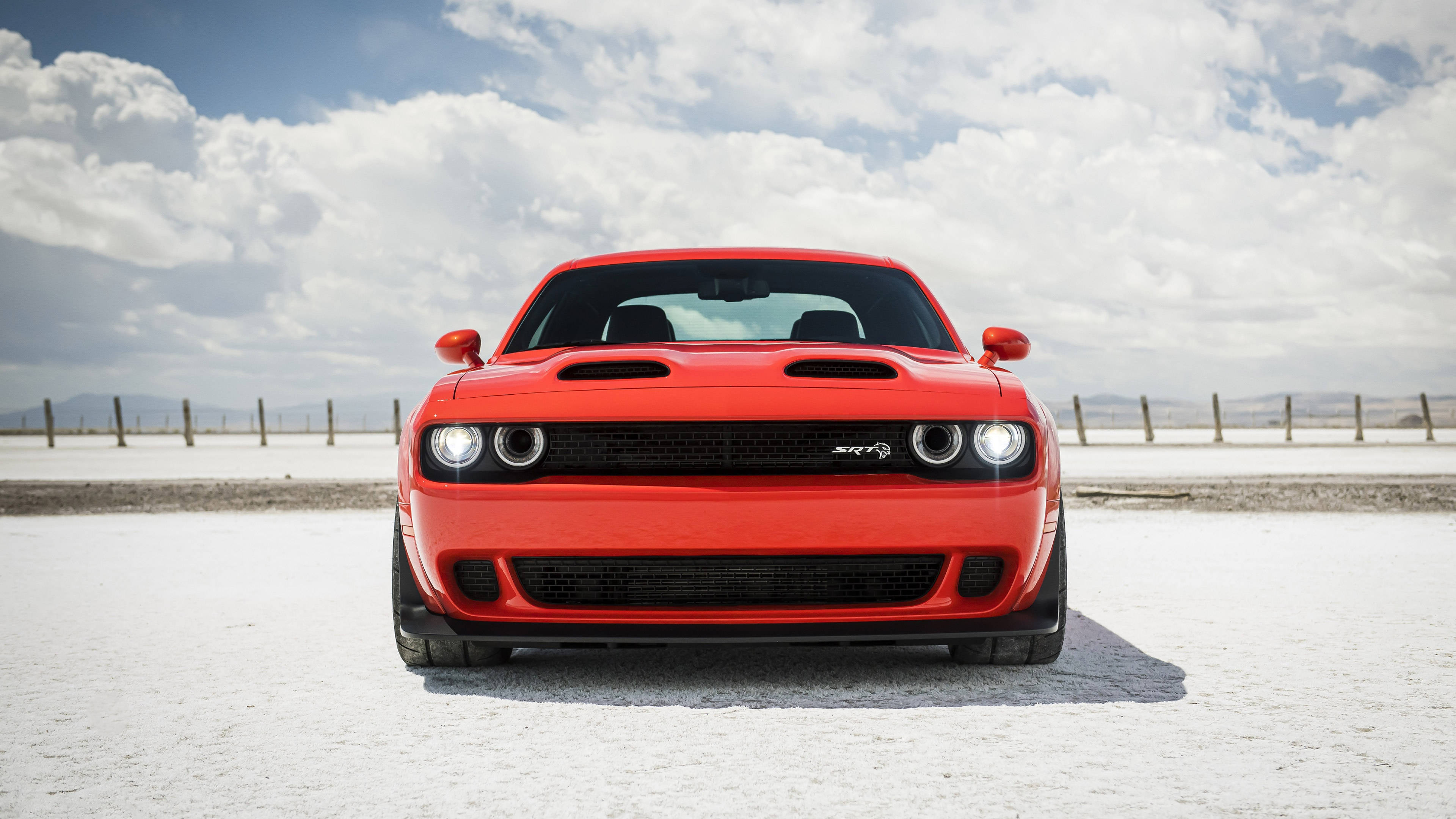 Challenger 桌布 壁紙 — 一輛鮮紅色的 Dodge Challenger SRT Hellcat 在廣闊的白色鹽灘上向前行駛，背景是戲劇性的多雲天空。