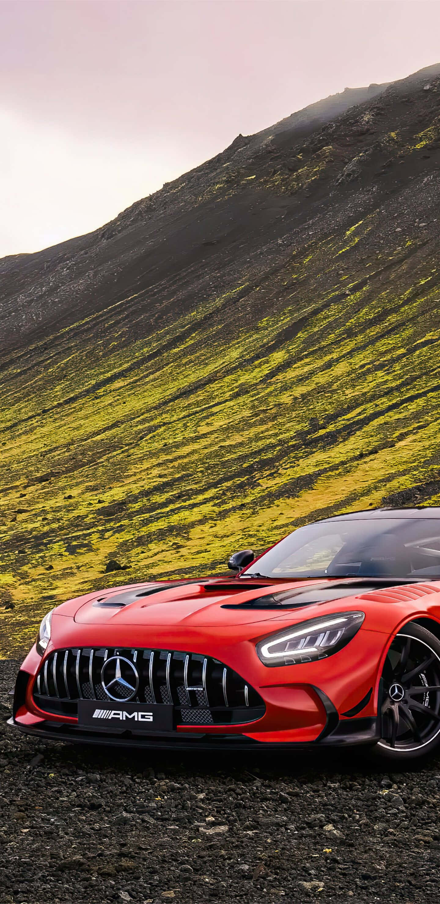 Red Car 桌布 壁紙 — 一輛鮮紅色的 Mercedes-AMG GT 停在碎石路上，前方是陡峭的山坡，覆蓋著綠色和黃色苔蘚的條紋，在柔和日光下。