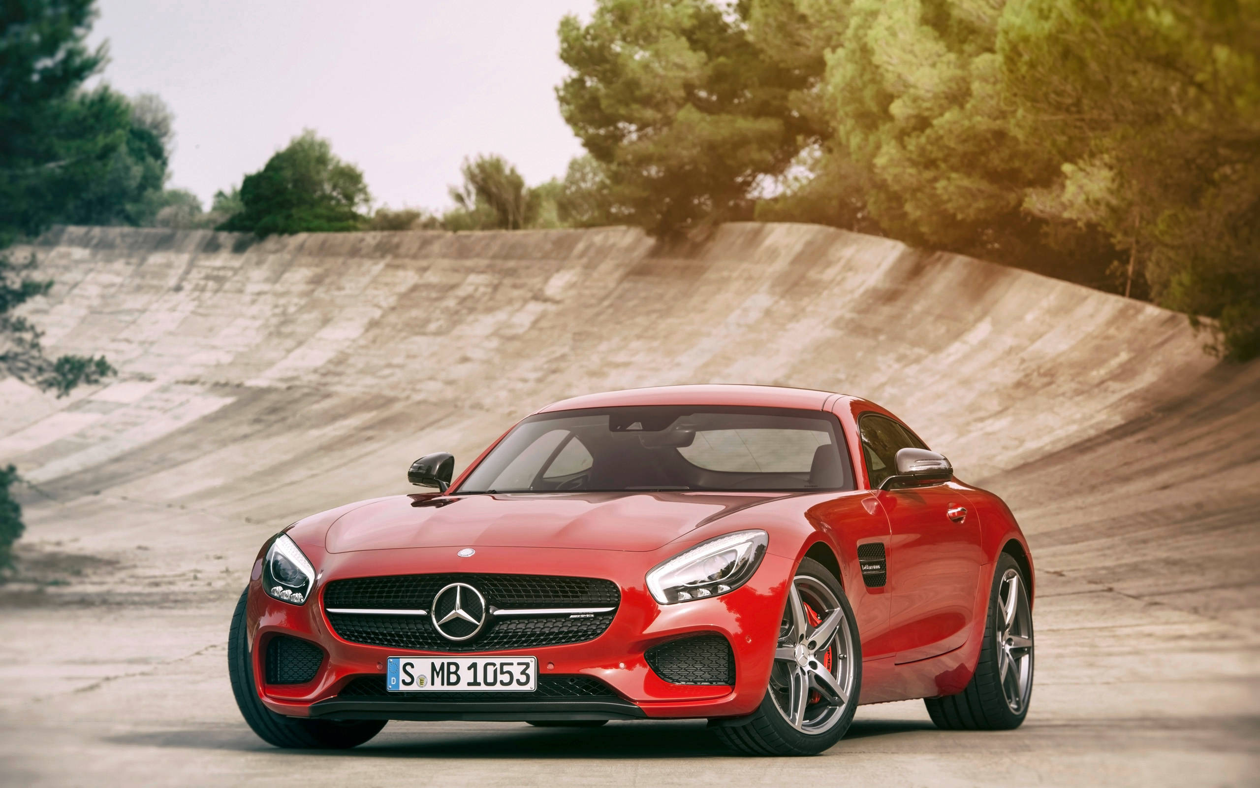 Mercedes Benz Amg 桌布 壁紙 — 一輛鮮紅色的 Mercedes-AMG GT 跑車停放在彎曲的混凝土坡道上，周圍綠樹環繞。