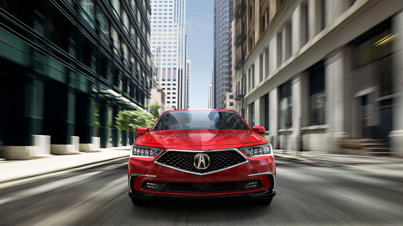 Acura Rlx 桌布 壁紙 — 一輛鮮紅色的Acura轎車在陽光明媚的城市街道上飛馳，兩旁是高聳的摩天大樓和歷史建築。