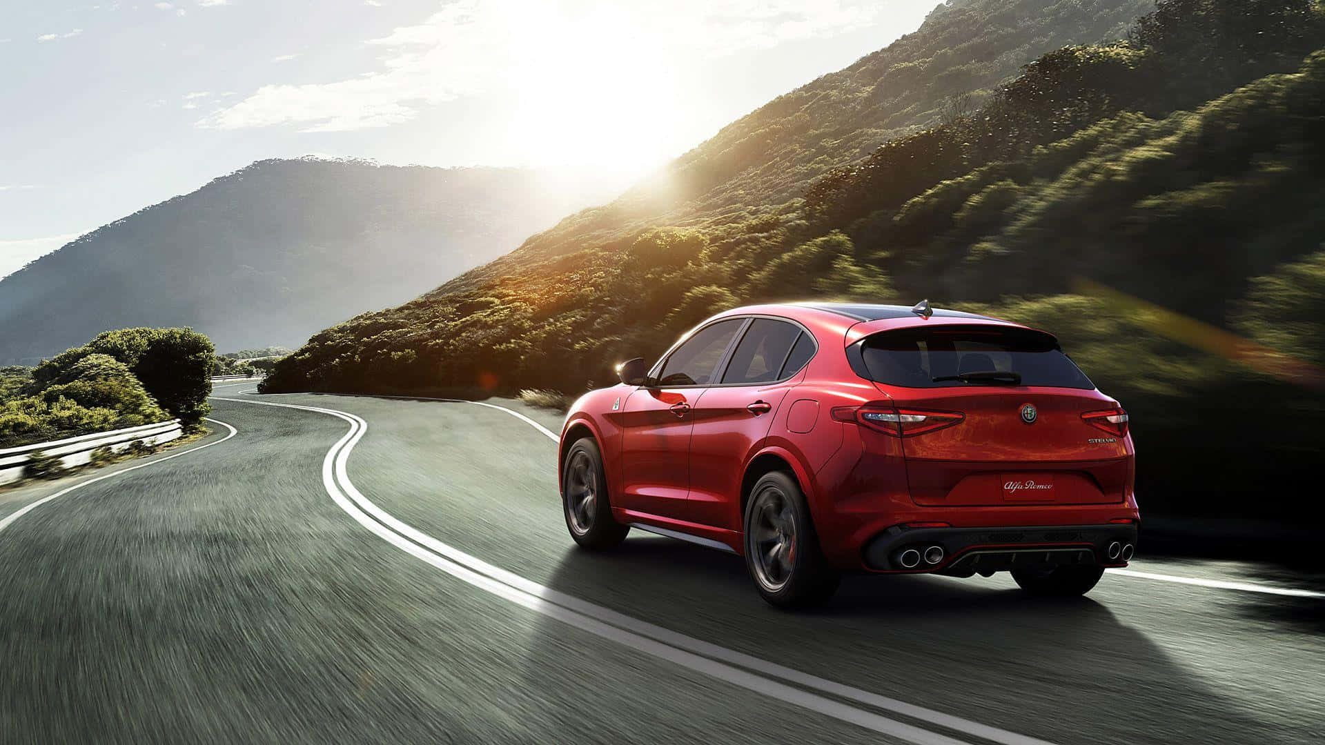 Alfa Romeo Stelvio 桌布 壁紙 — 一輛鮮紅色的Alfa Romeo SUV在沐浴在金色日落光線中的蜿蜒山路上飛馳。
