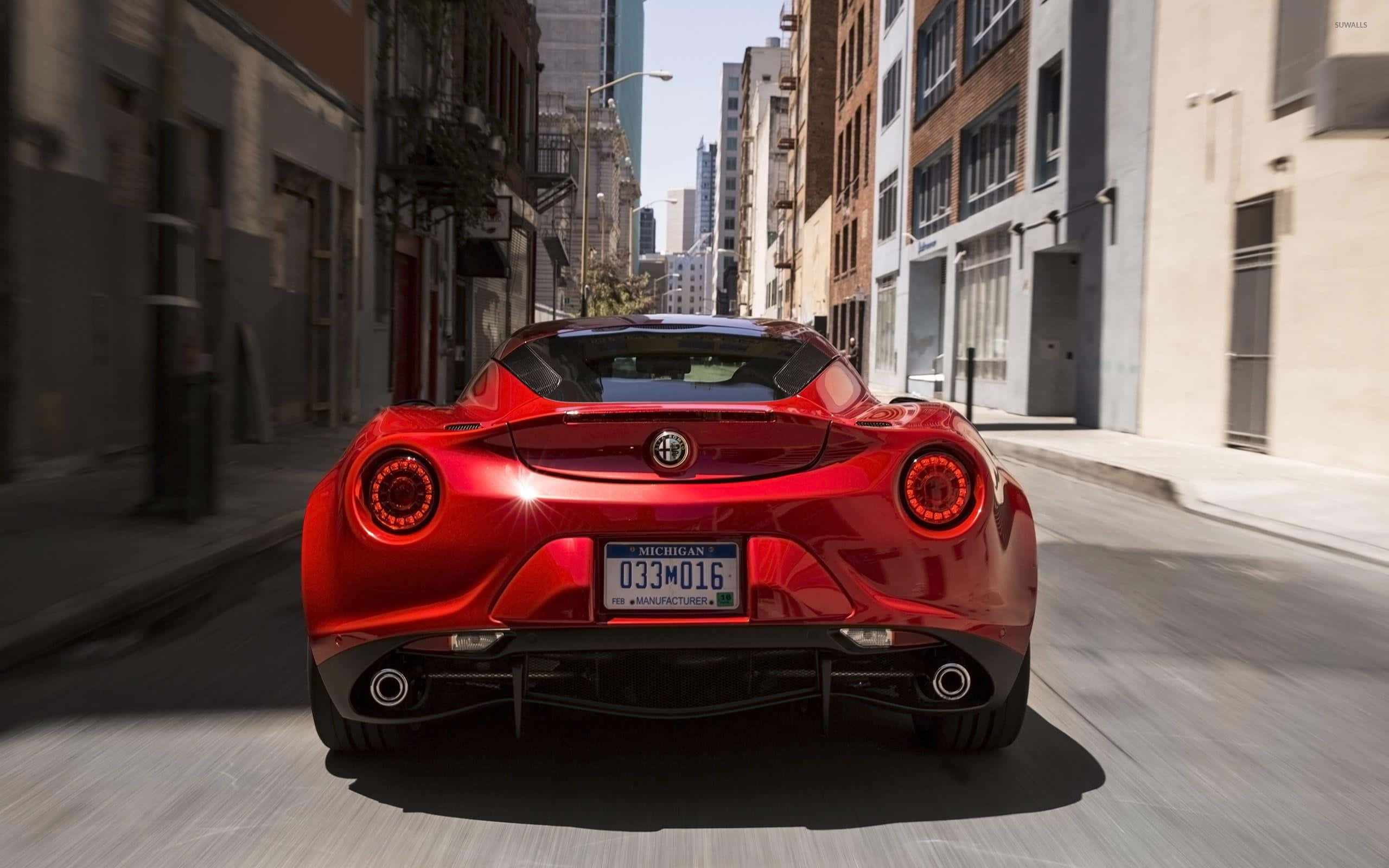 Alfa Romeo 4c 桌布 壁紙 — 一輛鮮紅色的Alfa Romeo跑車在陽光明媚的城市街道上飛馳，動態模糊強調了其動感十足的運動。