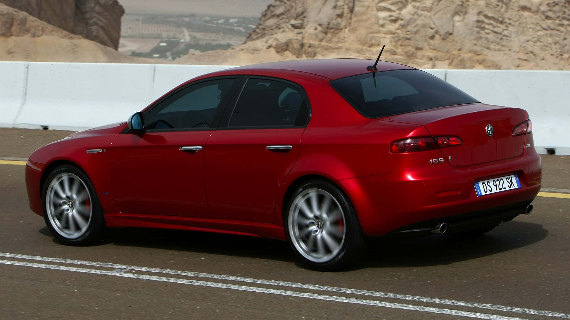 Alfa Romeo 159 桌布 壁紙 — 一輛鮮紅色的Alfa Romeo 159房車在沙漠公路上行駛，背景是岩石峭壁。