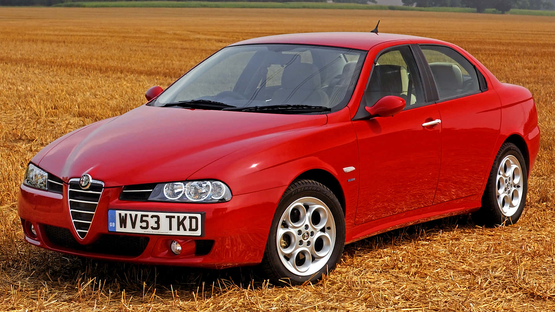 Alfa Romeo 156 桌布 壁紙 — 一輛鮮紅色的Alfa Romeo轎車停放在金色麥田中，在明亮的日光下。