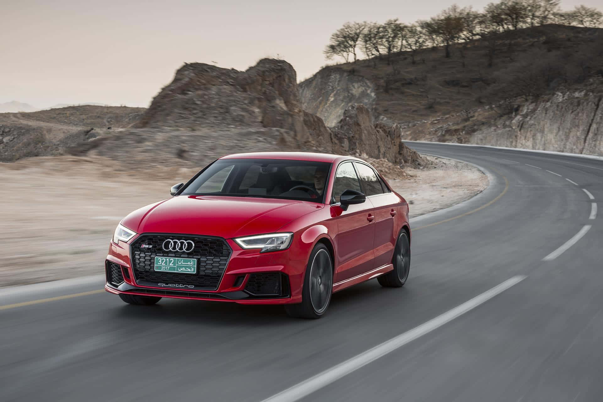 Audi Rs3 桌布 壁紙 — 一輛鮮紅色的Audi房車在蜿蜒的沙漠公路上疾馳，背景是岩石丘陵。
