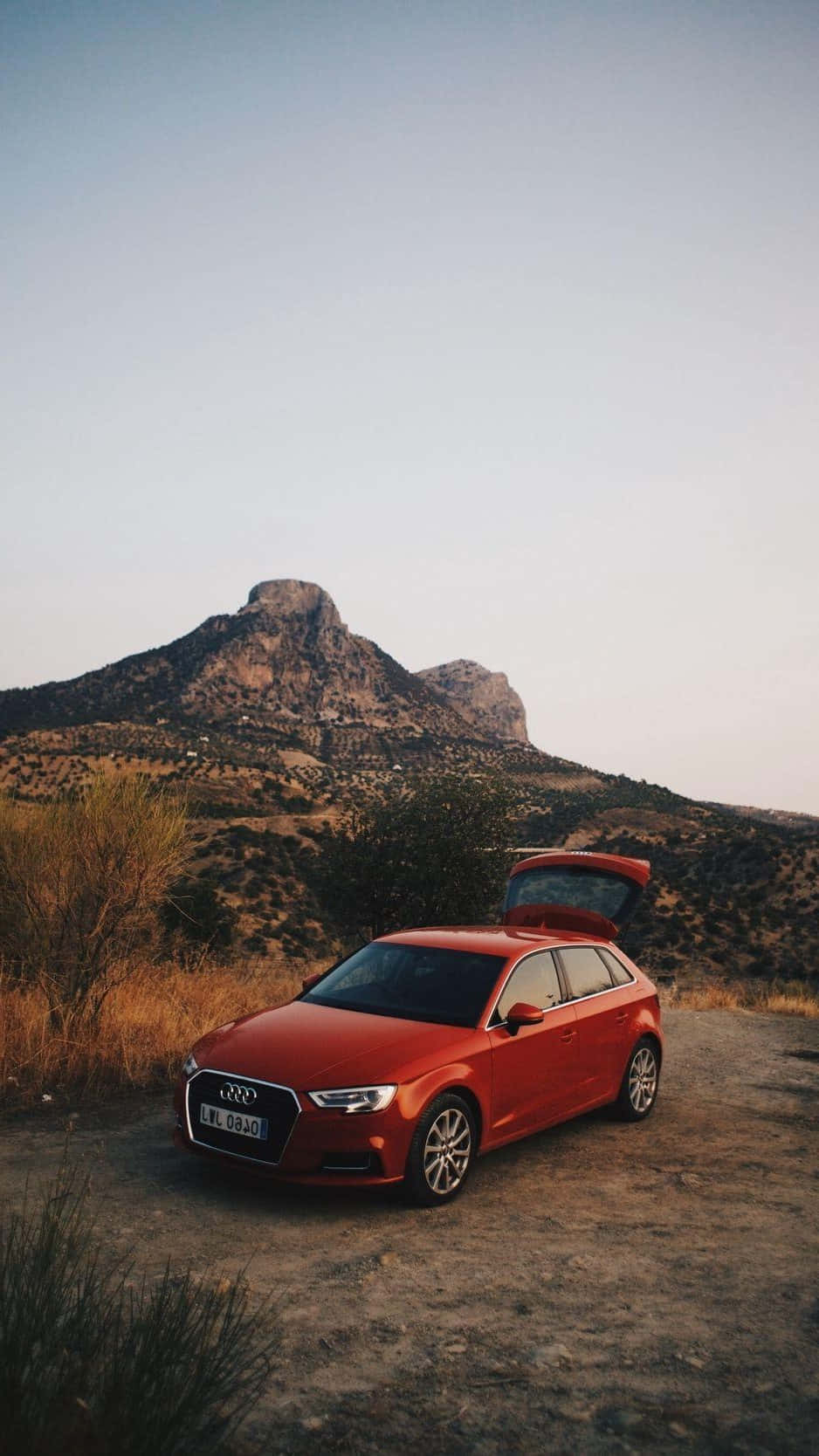 Audi Q5 桌布 壁紙 — 一輛鮮紅色的Audi旅行車停在塵土飛揚的小路上，後車門打開，背景是崎嶇的沙漠山脈，正值黃金時段。