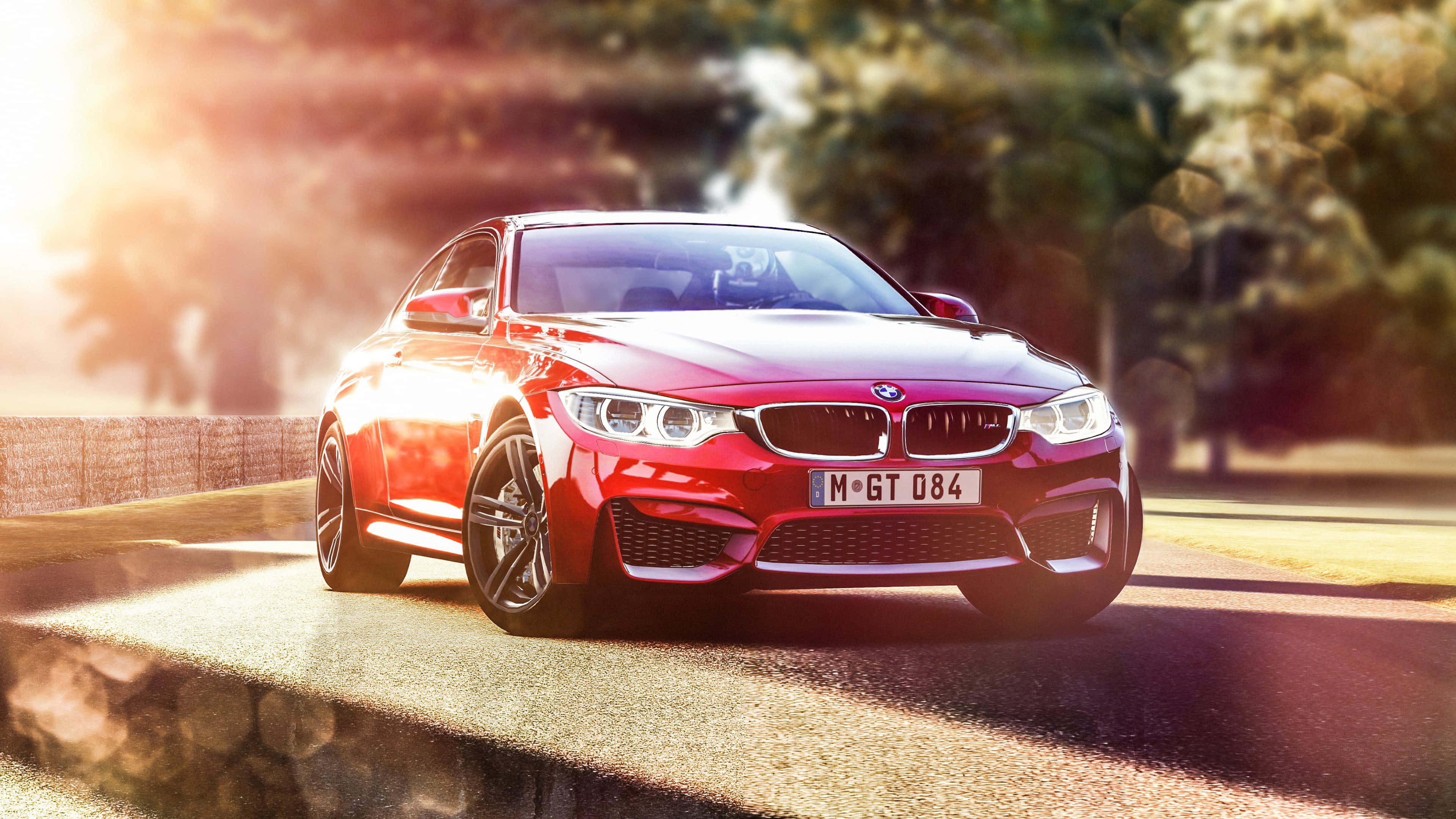 BMW 動圖 桌布 壁紙 — 一輛鮮紅色的BMW M4 GT4跑車在陽光明媚的賽道上疾馳，背景有模糊的樹木和溫暖的鏡頭光暈。