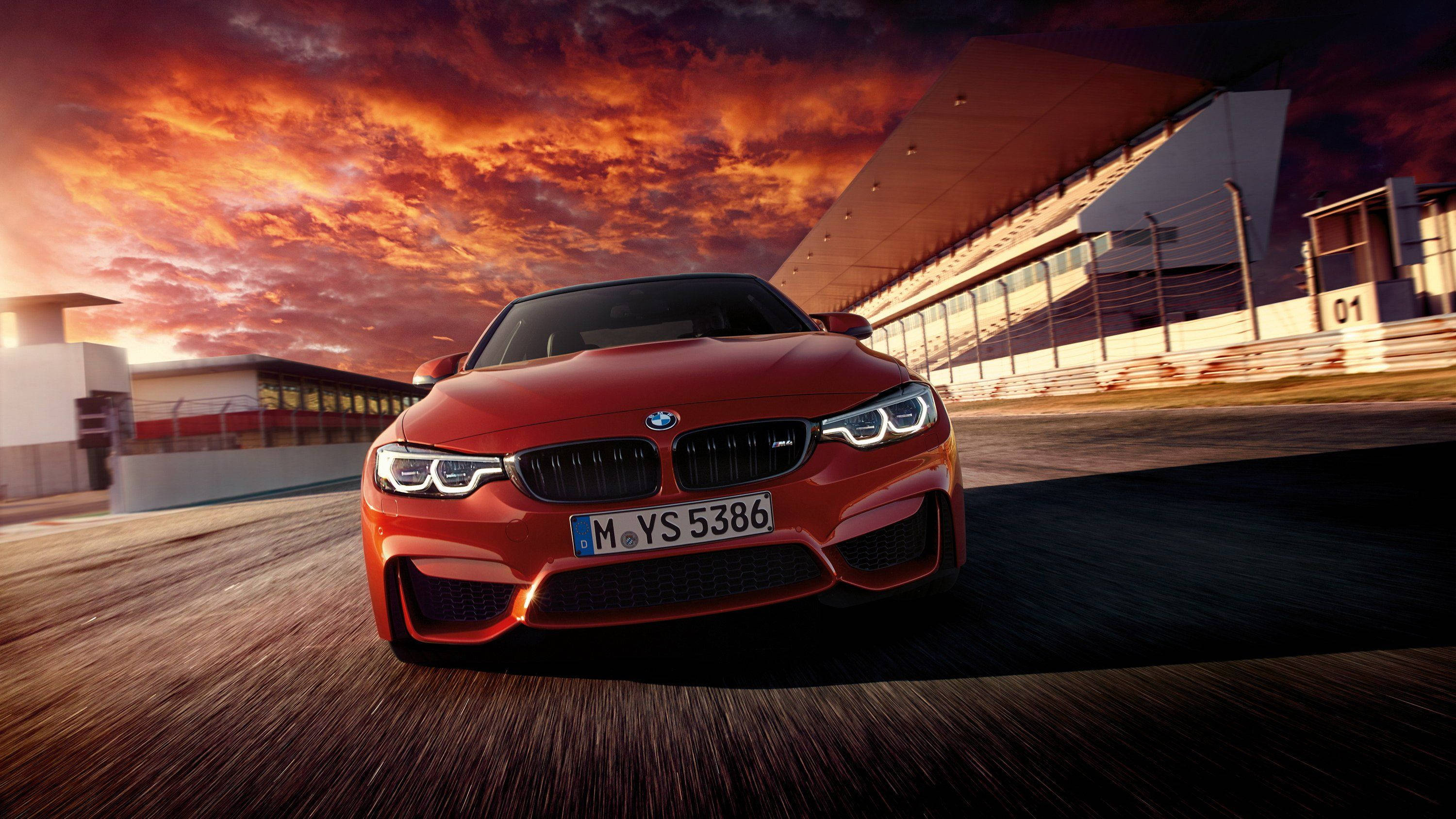BMW 動圖 桌布 壁紙 — 一輛鮮紅色的BMW M4在火紅橙紅色的日落天空下於賽道上奔馳。