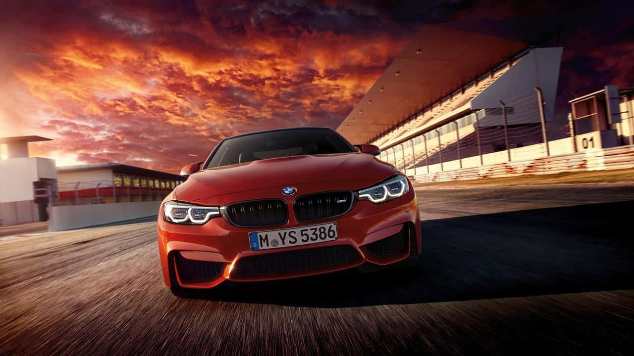 Cool Bmw 桌布 壁紙 — 一輛鮮紅色的BMW M4在火紅的橙色和紫色日落天空下沿著賽道飛馳。