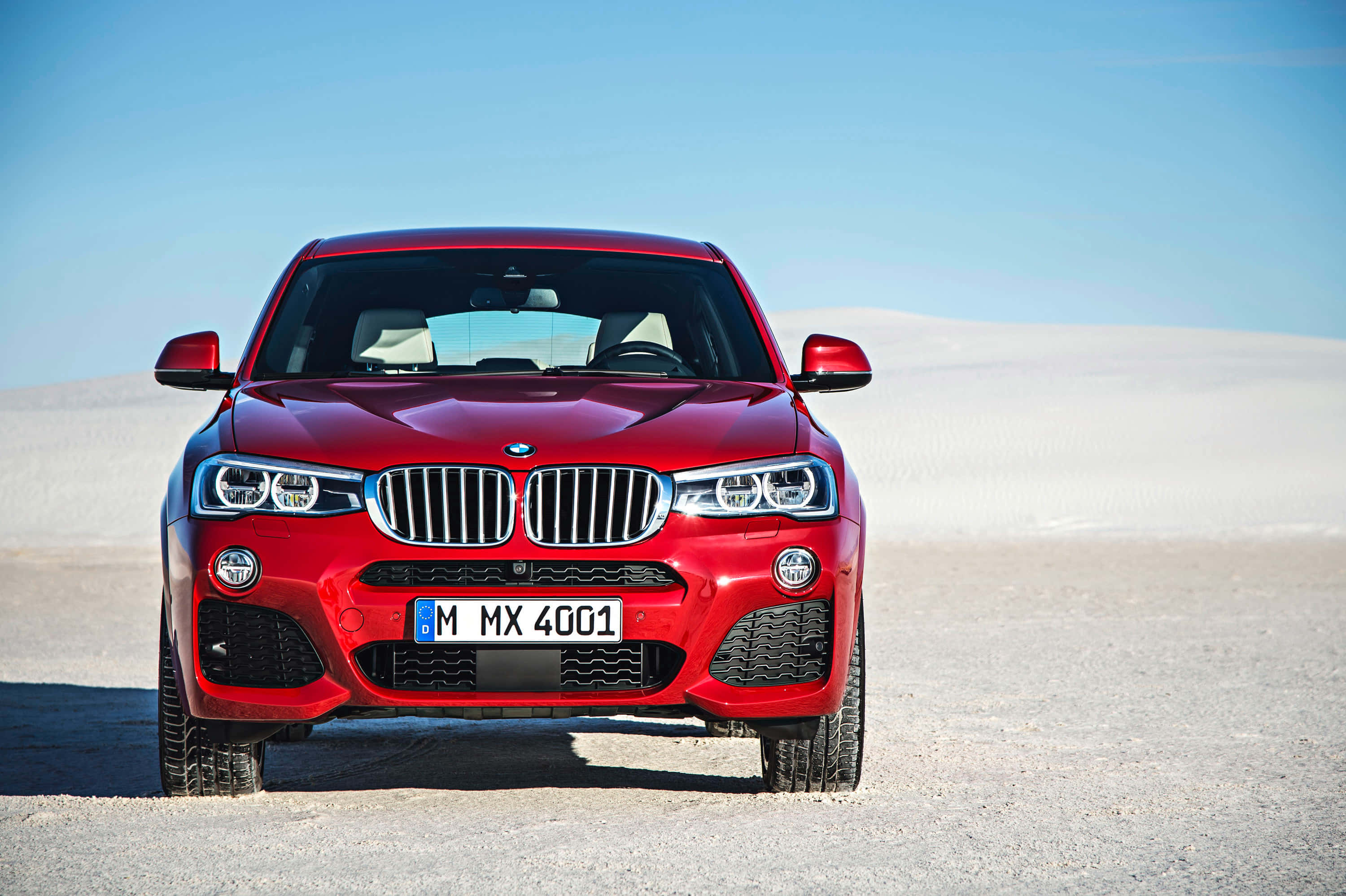 Bmw X4 桌布 壁紙 — 一輛鮮紅色的BMW X4 M在晴朗藍天下，勇敢地矗立在陽光普照的沙漠平原上。
