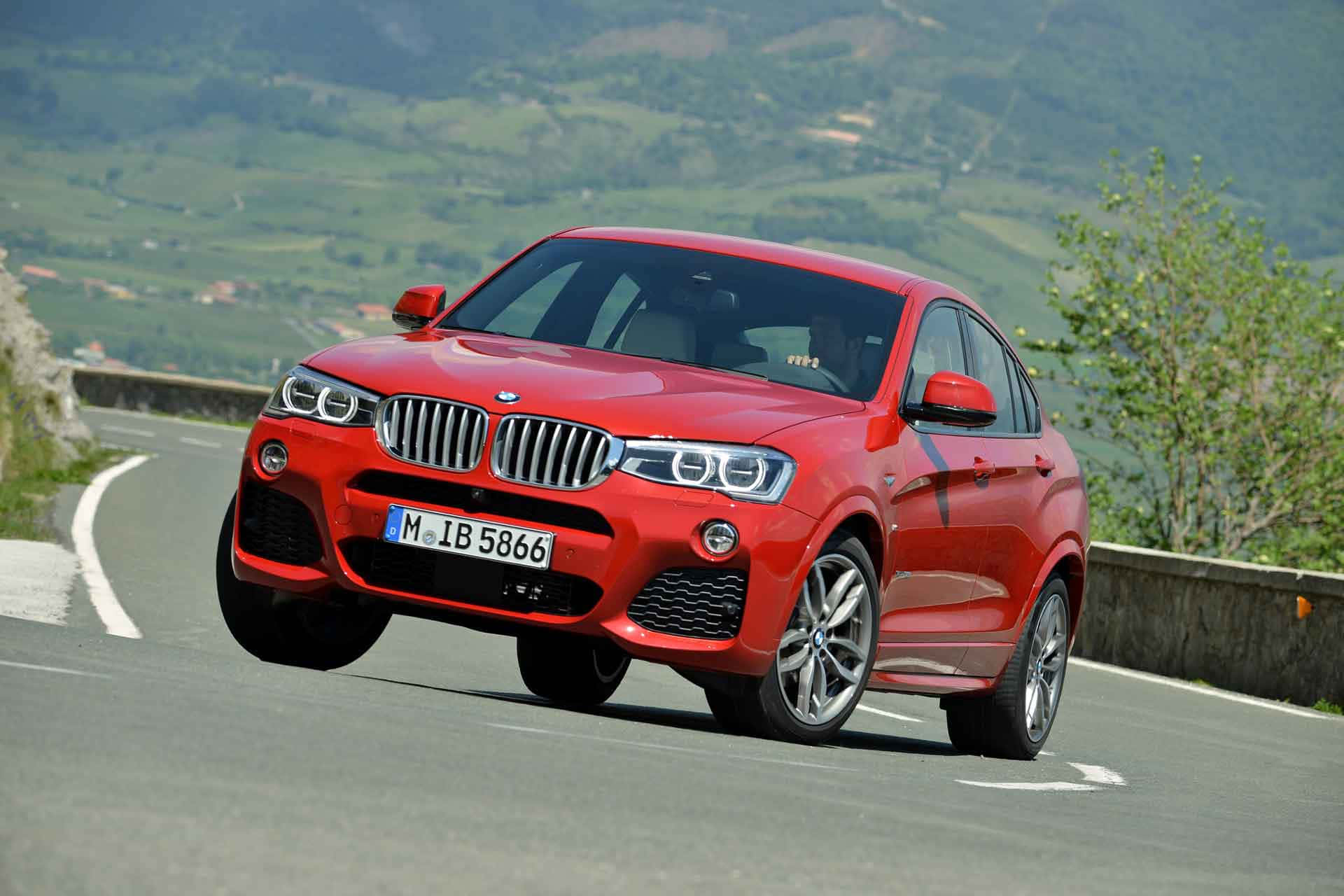 Bmw X4 桌布 壁紙 — 一輛鮮紅色的BMW X4 SUV在蜿蜒的山路上動態過彎，背景是鬱鬱蔥蔥的綠色山丘。