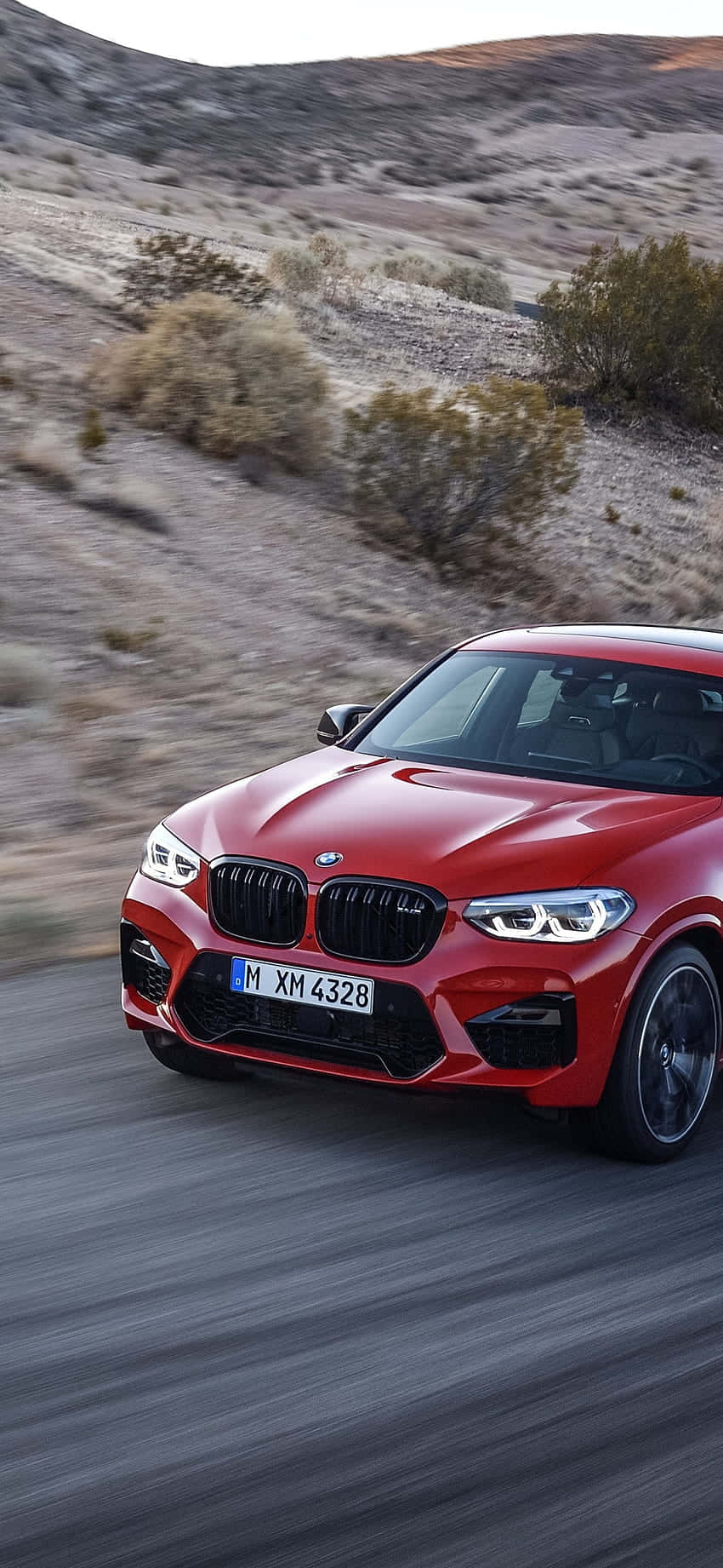 iPhone X M Series 桌布 壁紙 — 一輛鮮紅色的BMW X4在沙漠公路上疾馳，背景是模糊的動感和岩石丘陵。