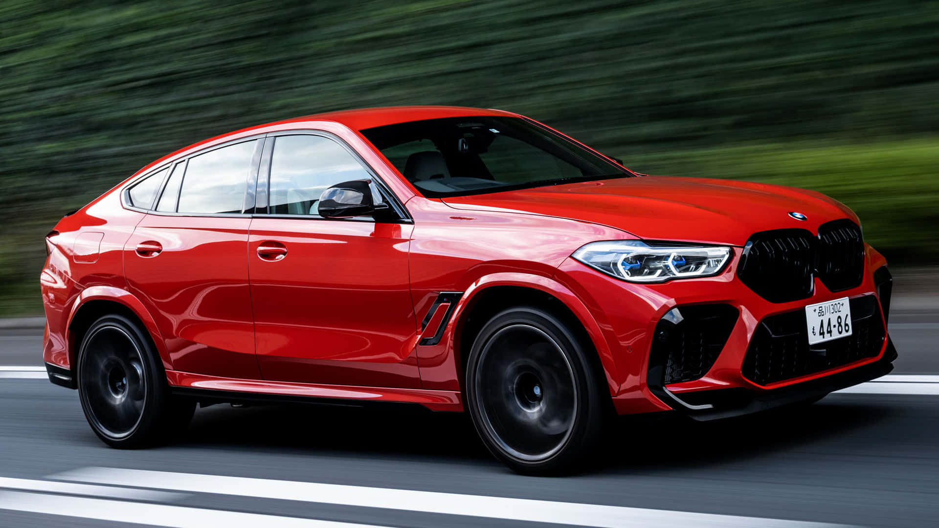 Bmw X6 M 桌布 壁紙 — 一輛鮮紅色的BMW X6 M在模糊的綠色背景中沿著道路疾馳。