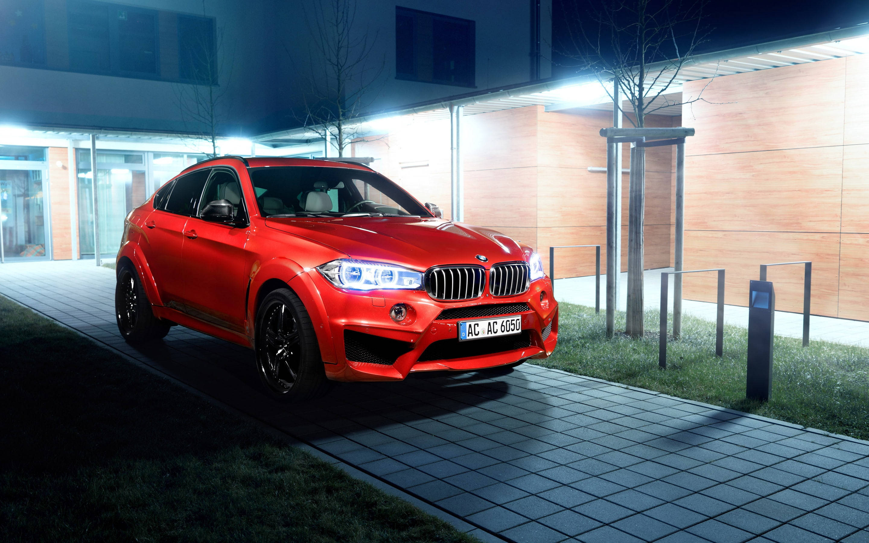 m 桌布 壁紙 — 一輛鮮紅色的BMW X6M AC Schnitzer在夜間停泊在現代建築旁邊的瓷磚行人路上，建築物有發光的燈光。