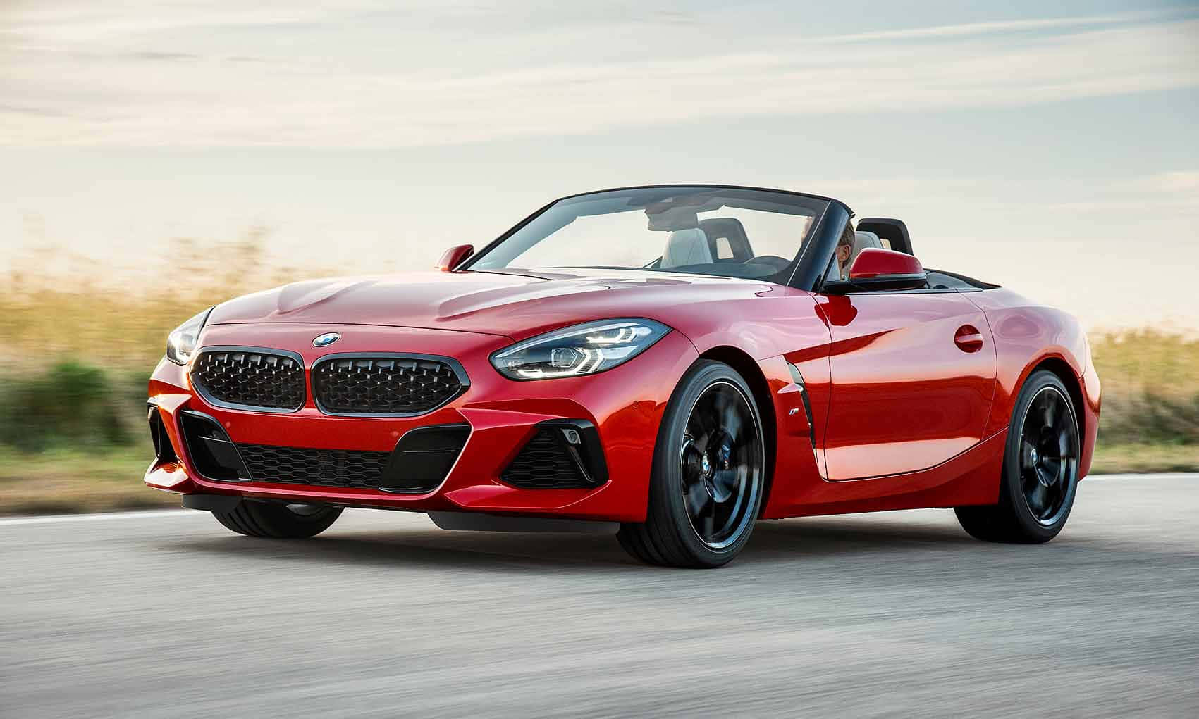 Bmw Z4 桌布 壁紙 — 一輛鮮紅色的BMW Z4敞篷跑車在柔和天空下，沿著一條有模糊金色草叢的道路飛馳。