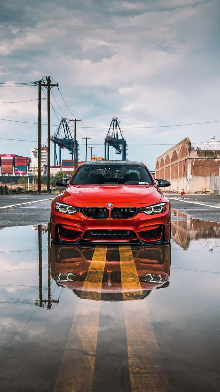 BMW 動圖 桌布 壁紙 — 一輛鮮紅色的BMW跑車倒映在潮濕工業街道的水坑中，天空多雲。