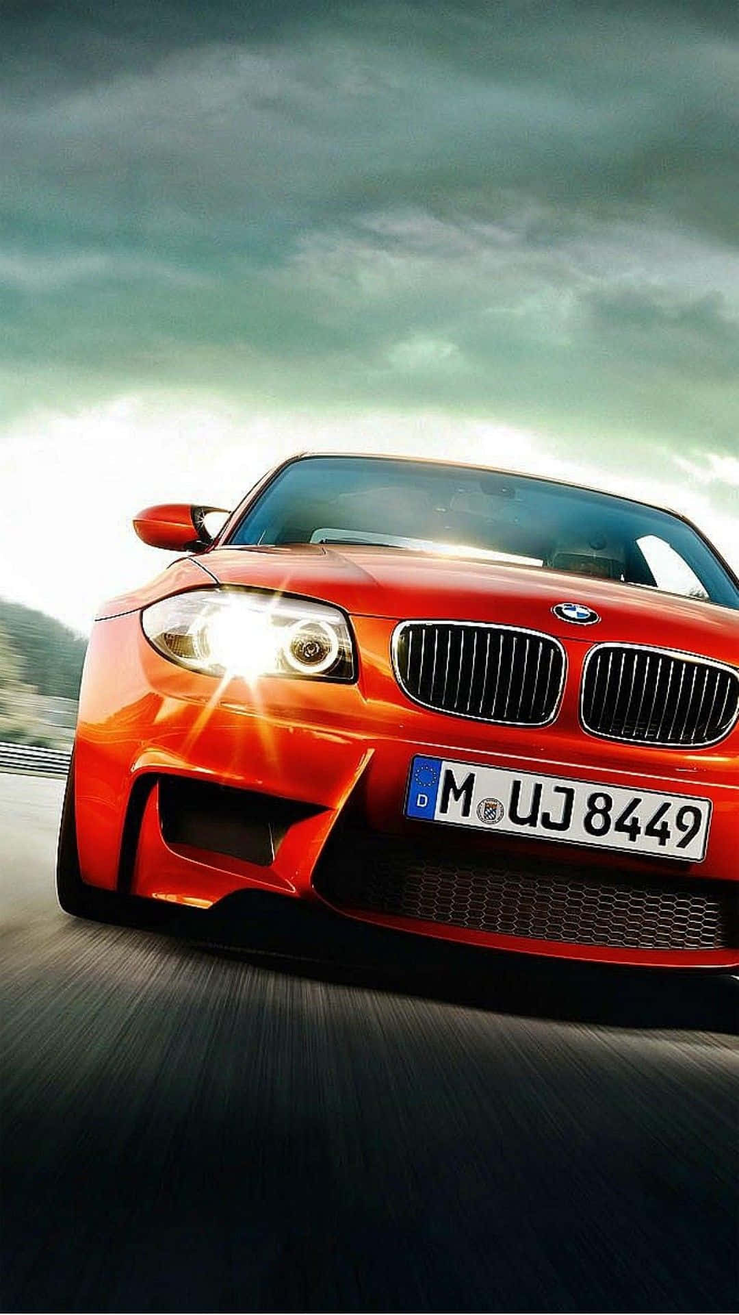 桌布 壁紙 — 一輛鮮紅色的BMW跑車在戲劇性的多雲天空下，在模糊的道路上疾馳前進。