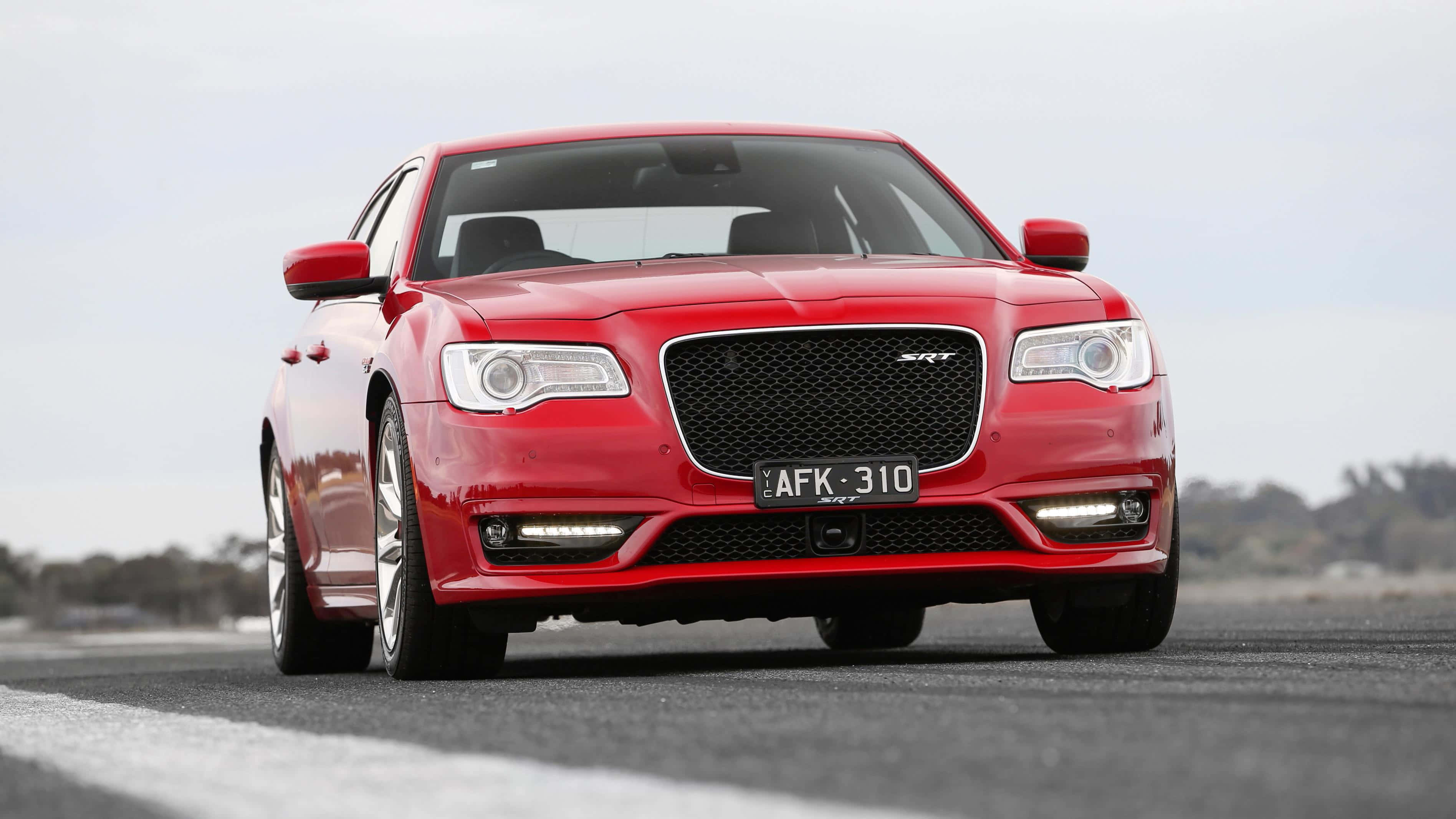 Chrysler 桌布 壁紙 — 一輛鮮紅色的Chrysler 300 SRT轎車在多雲的天空下，在開闊的柏油路上激進地向前傾斜。