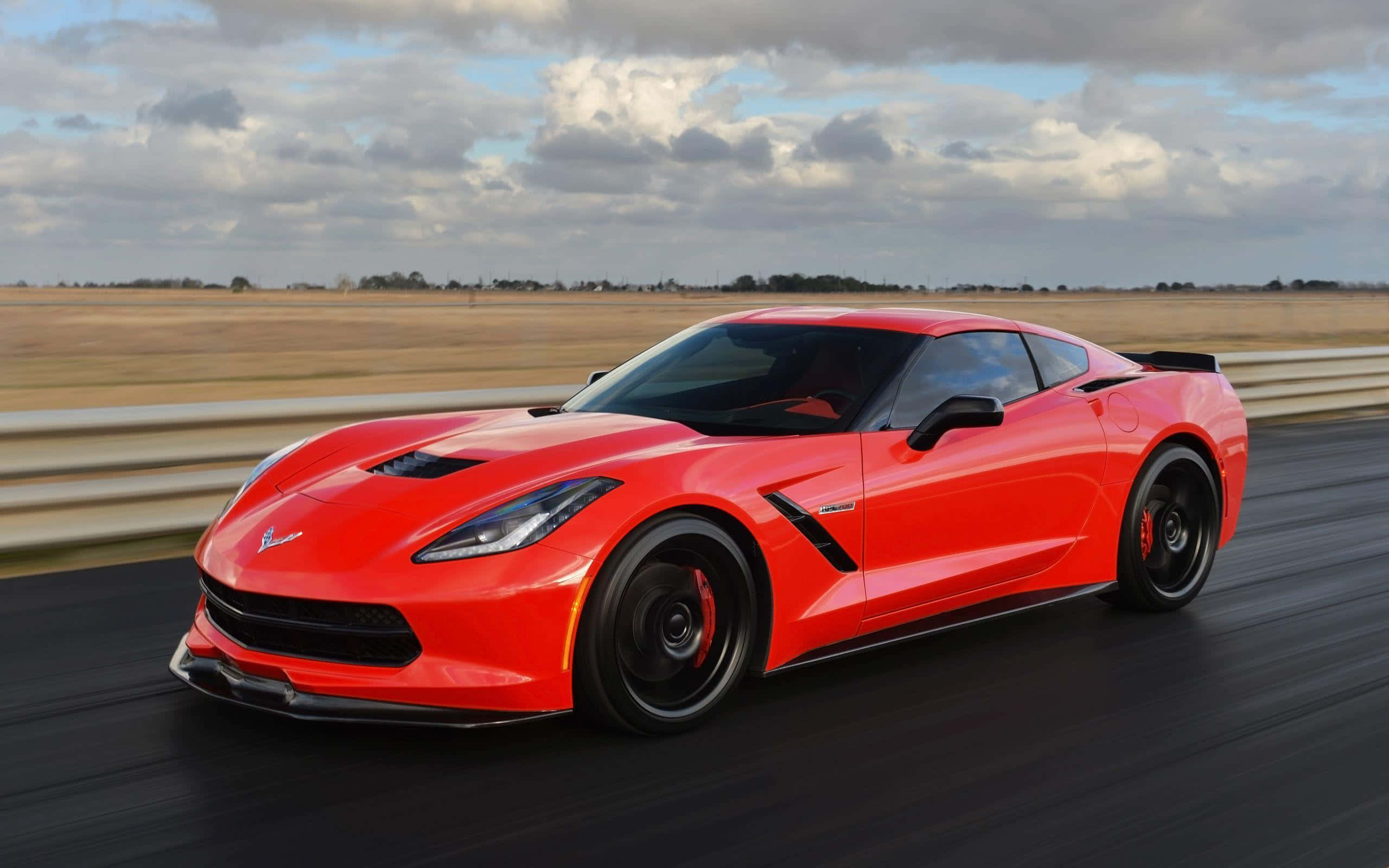 Chevrolet Corvette Stingray 桌布 壁紙 — 一輛鮮紅色的Corvette跑車在陰天天空下沿著賽道疾馳，帶有動態模糊效果。