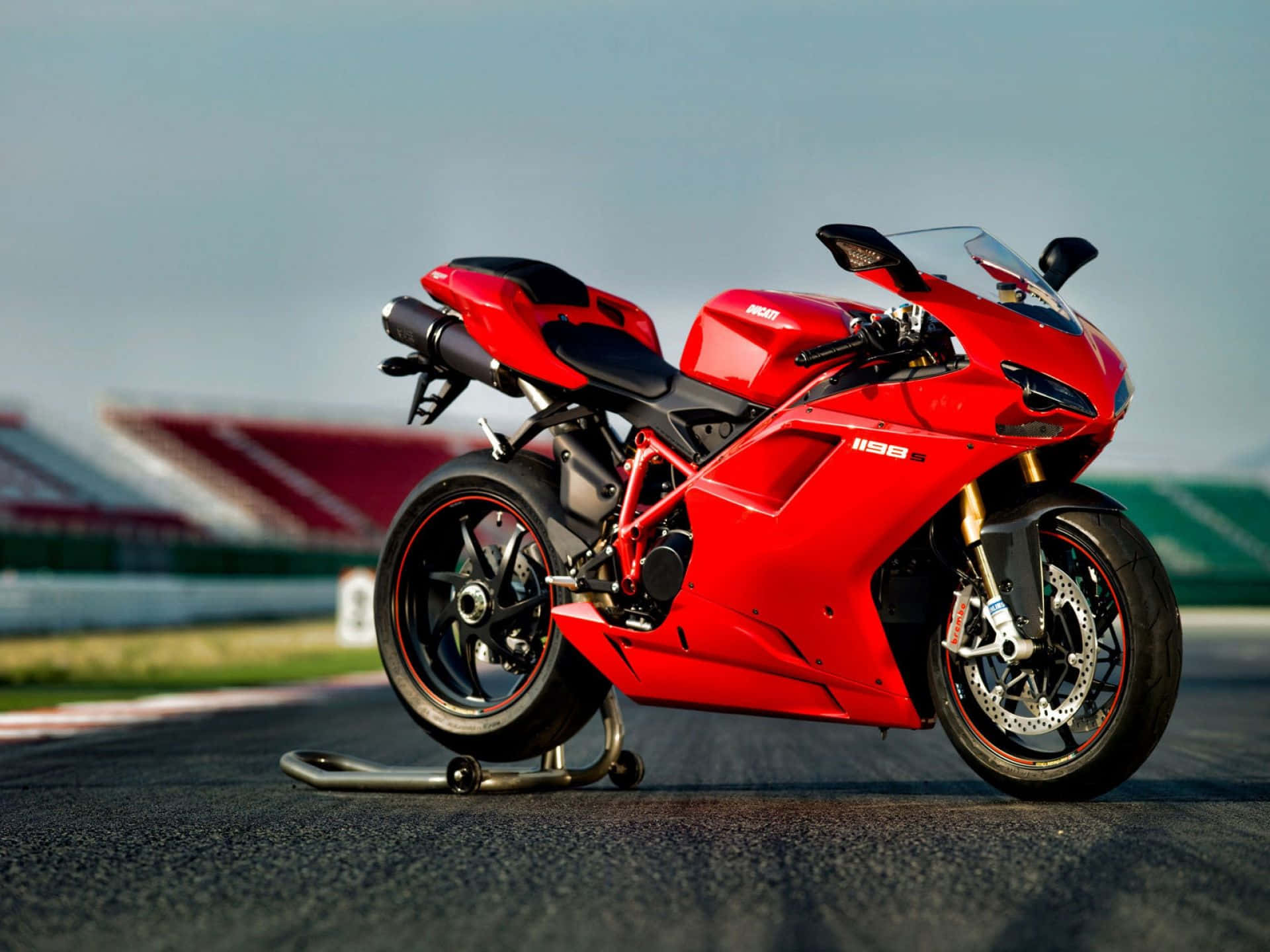 機車 桌布 壁紙 — 一輛鮮紅色的Ducati 1198摩托車在賽道上蓄勢待發，背景是模糊的看台。