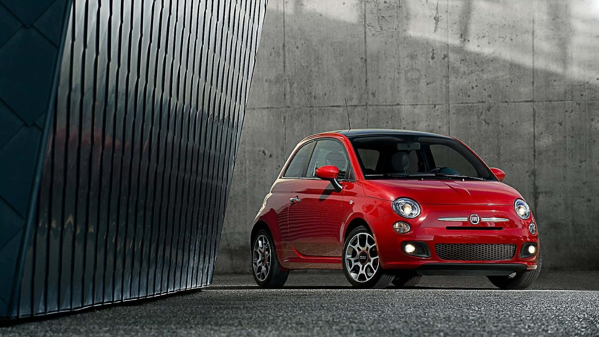 Fiat 500l 桌布 壁紙 — 一輛鮮紅色的Fiat 500停放在深色波紋牆和混凝土之間，在明亮的日光下投下清晰的陰影。