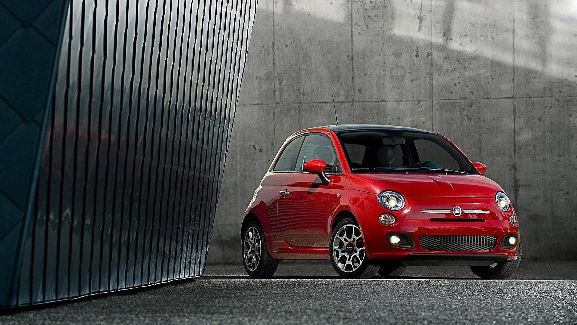 Fiat 桌布 壁紙 — 一輛鮮紅色的Fiat 500停放在光滑的深色牆壁和紋理混凝土背景之間。