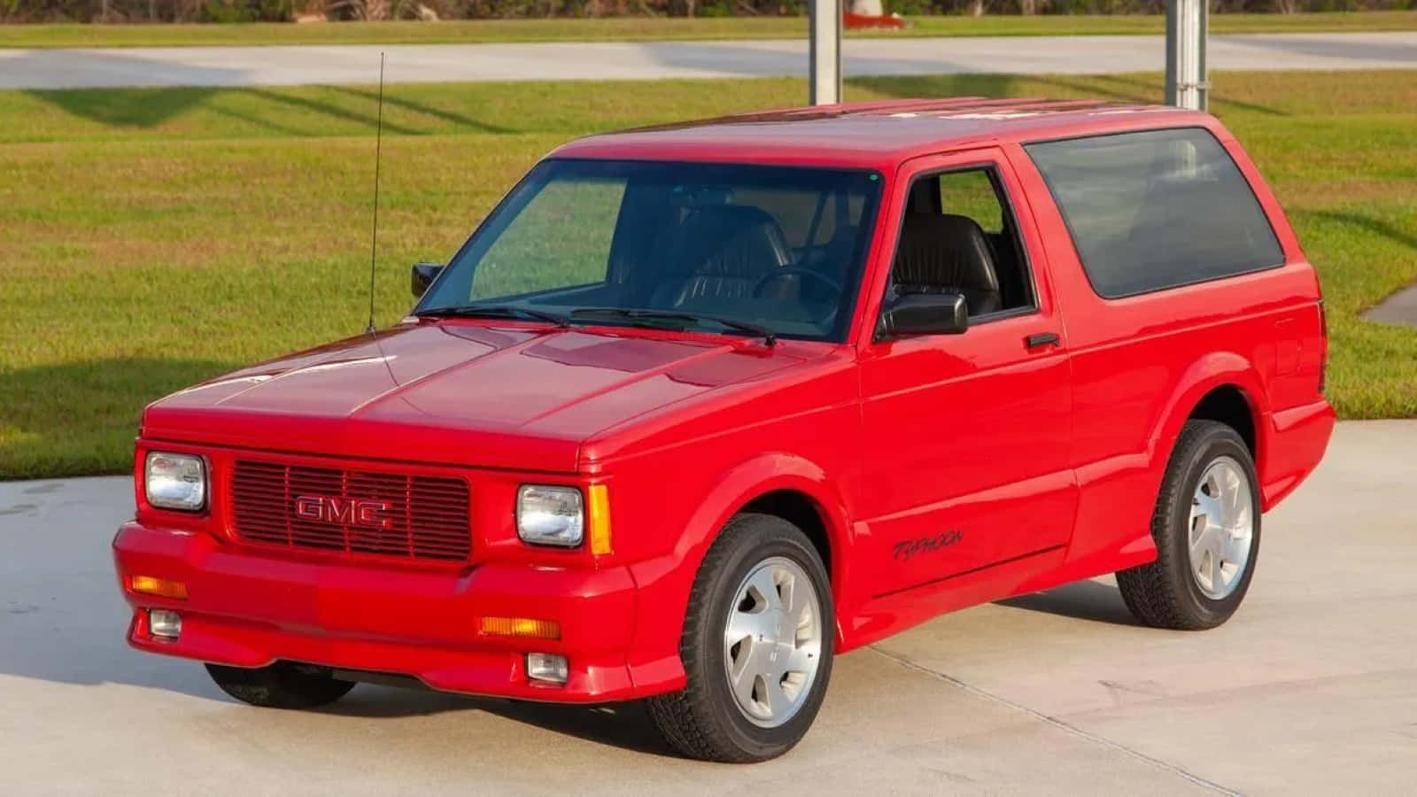 Gmc Typhoon 桌布 壁紙 — 一輛鮮紅色的GMC Typhoon運動型多功能車停在混凝土車道上，背景有草地和道路。