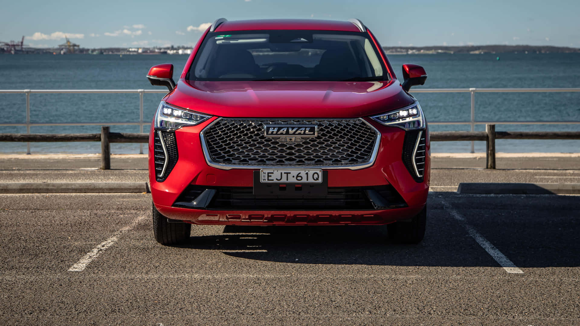 Haval 桌布 壁紙 — 一輛鮮紅色的Haval SUV停泊在海邊碼頭，平靜的藍色大海和遠處城市景觀，天空晴朗。