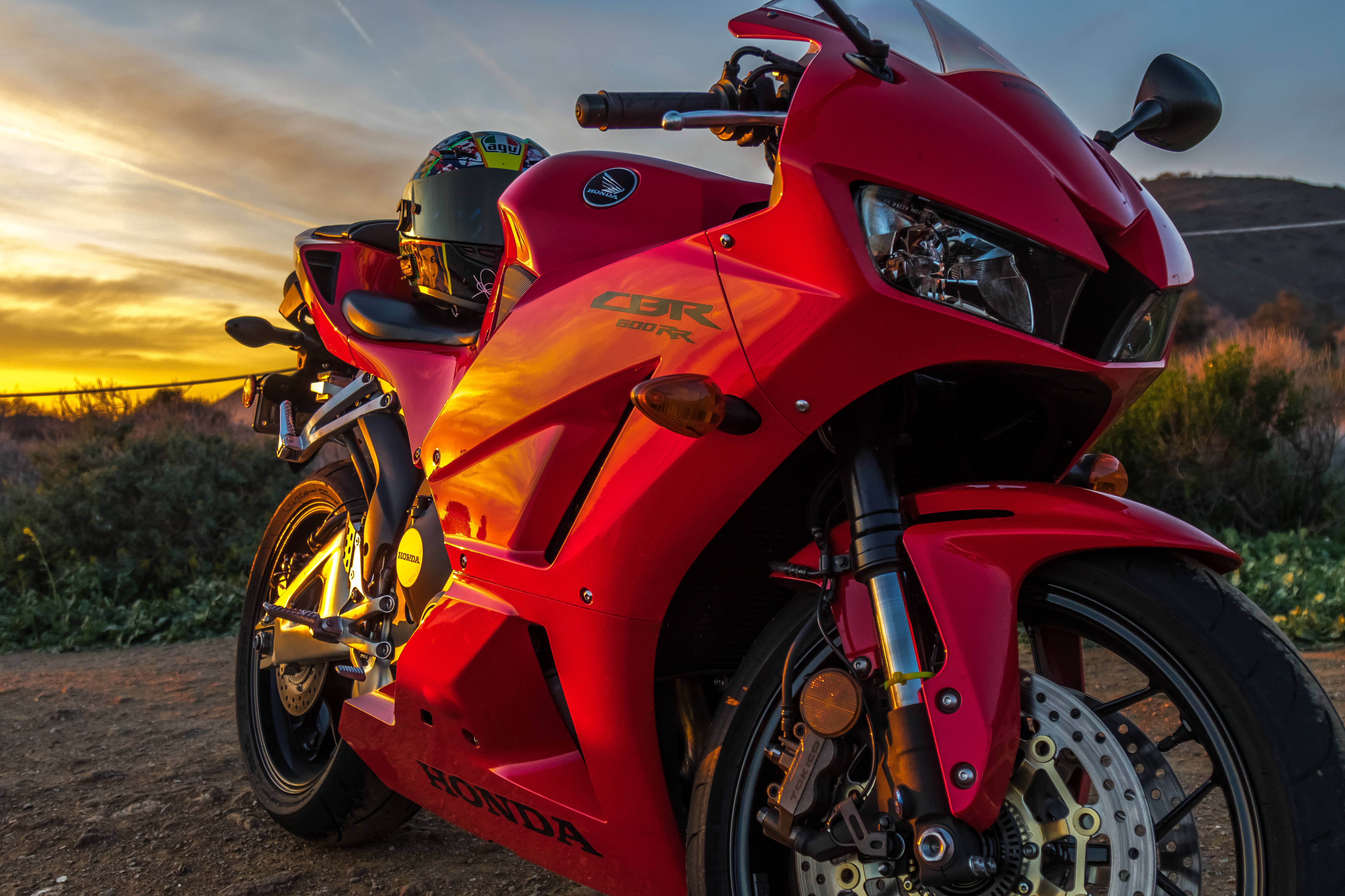  壁紙 — 一輛鮮紅色的Honda CBR 600 RR跑車在金色夕陽下閃閃發光，停在一條泥土路上，背景是山丘。