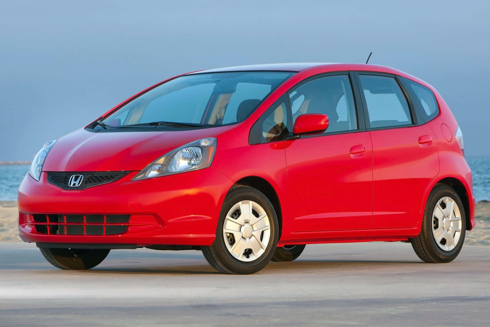 Honda Fit 桌布 壁紙 — 一輛鮮紅色的Honda Fit停泊在沙灘上，背景是海浪和柔和的藍天。